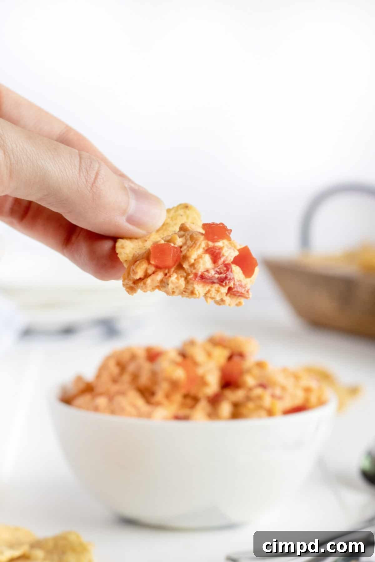A large bowl of Pimento Cheese Dip placed centrally on a rustic wooden board, artfully arranged with various dipping options like crackers, celery sticks, and different types of chips, perfect for a party.
