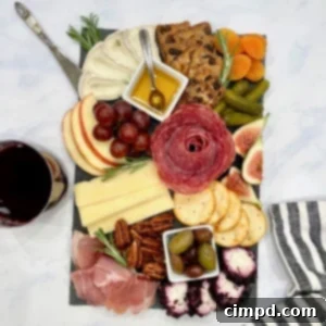 A small wooden board with meats, cheeses, apple slices, red grapes, an assortment of olives and crackers.