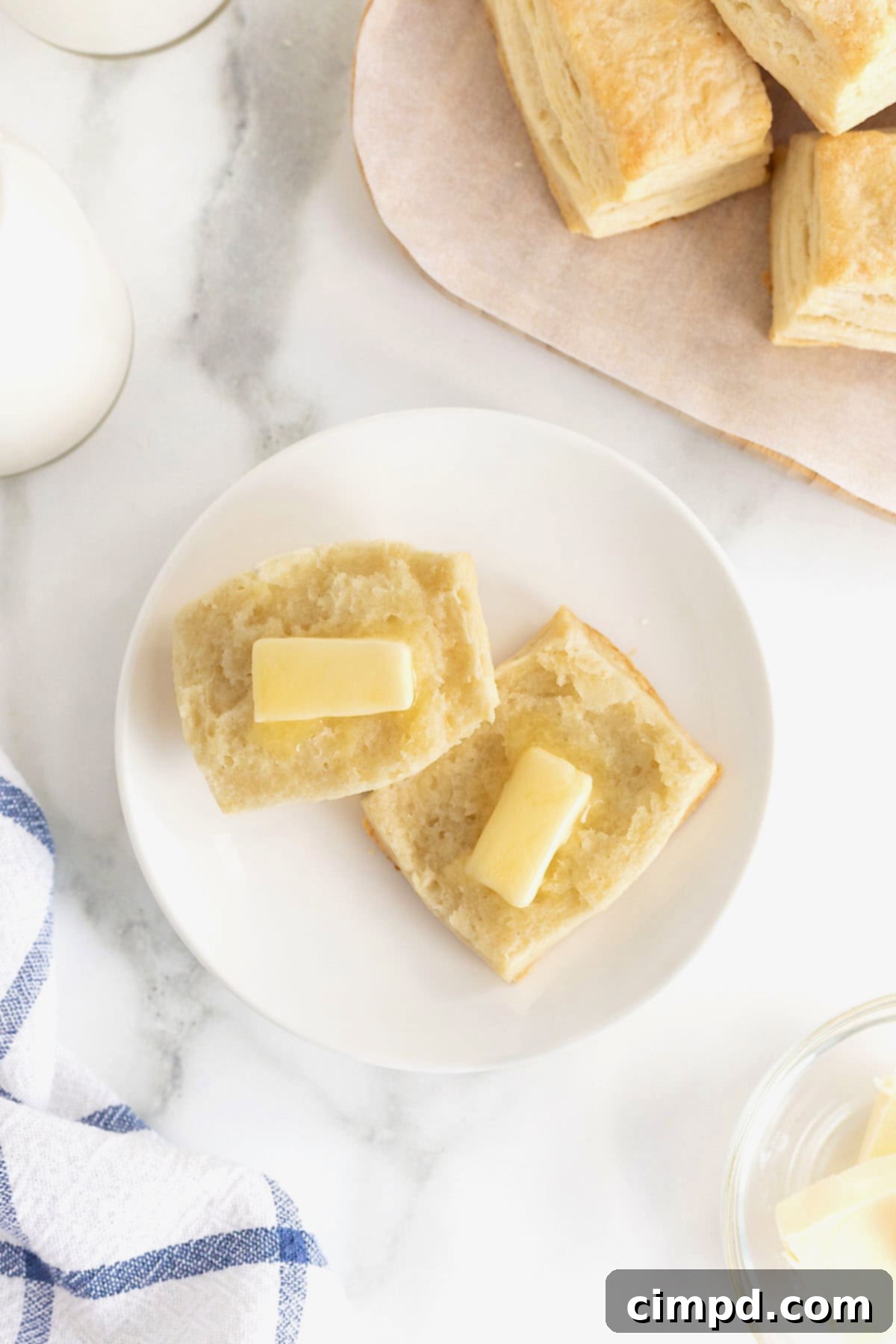 Comforting Buttermilk Biscuits 4 A warm, freshly baked buttermilk biscuit sliced cleanly in half, revealing its tender, layered interior, with a generous pat of butter melting into each half.