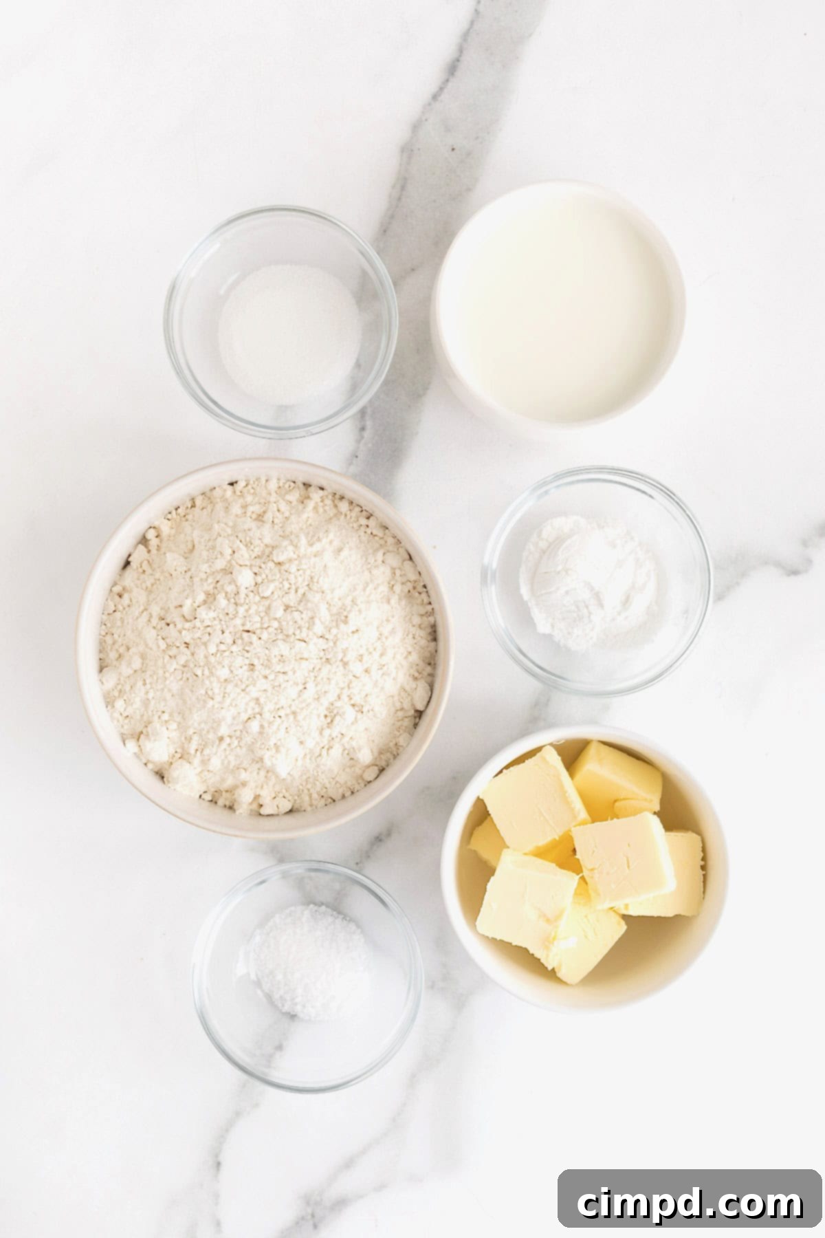 Comforting Buttermilk Biscuits 7 Individual glass dishes filled with the essential ingredients for homestyle buttermilk biscuits, neatly arranged on a pristine white marble counter, ready for baking.