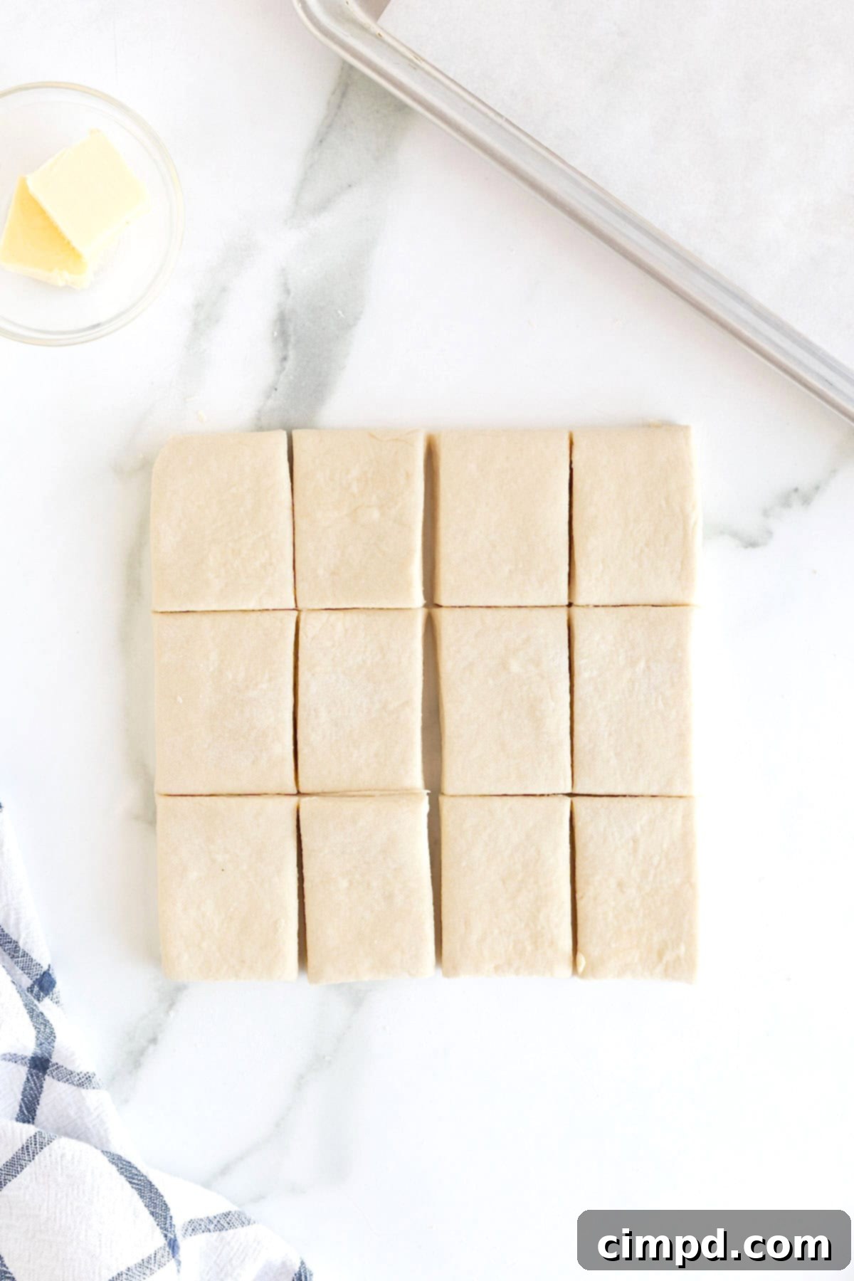 Comforting Buttermilk Biscuits 10 Twelve perfectly cut square buttermilk biscuit dough pieces neatly arranged on a floured white marble counter, ready for the baking sheet.