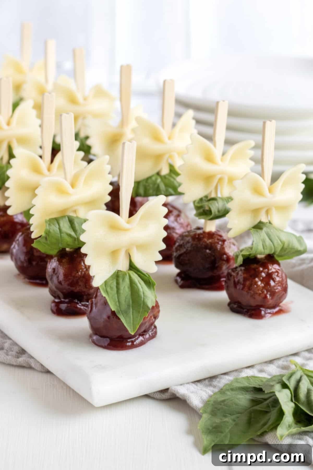 A stunning overhead view of 12 wooden skewers, each artfully composed with bowtie pasta and succulent meatballs, presented on a elegant white marble serving plate. The arrangement is both inviting and visually appealing, promising a delicious culinary experience.