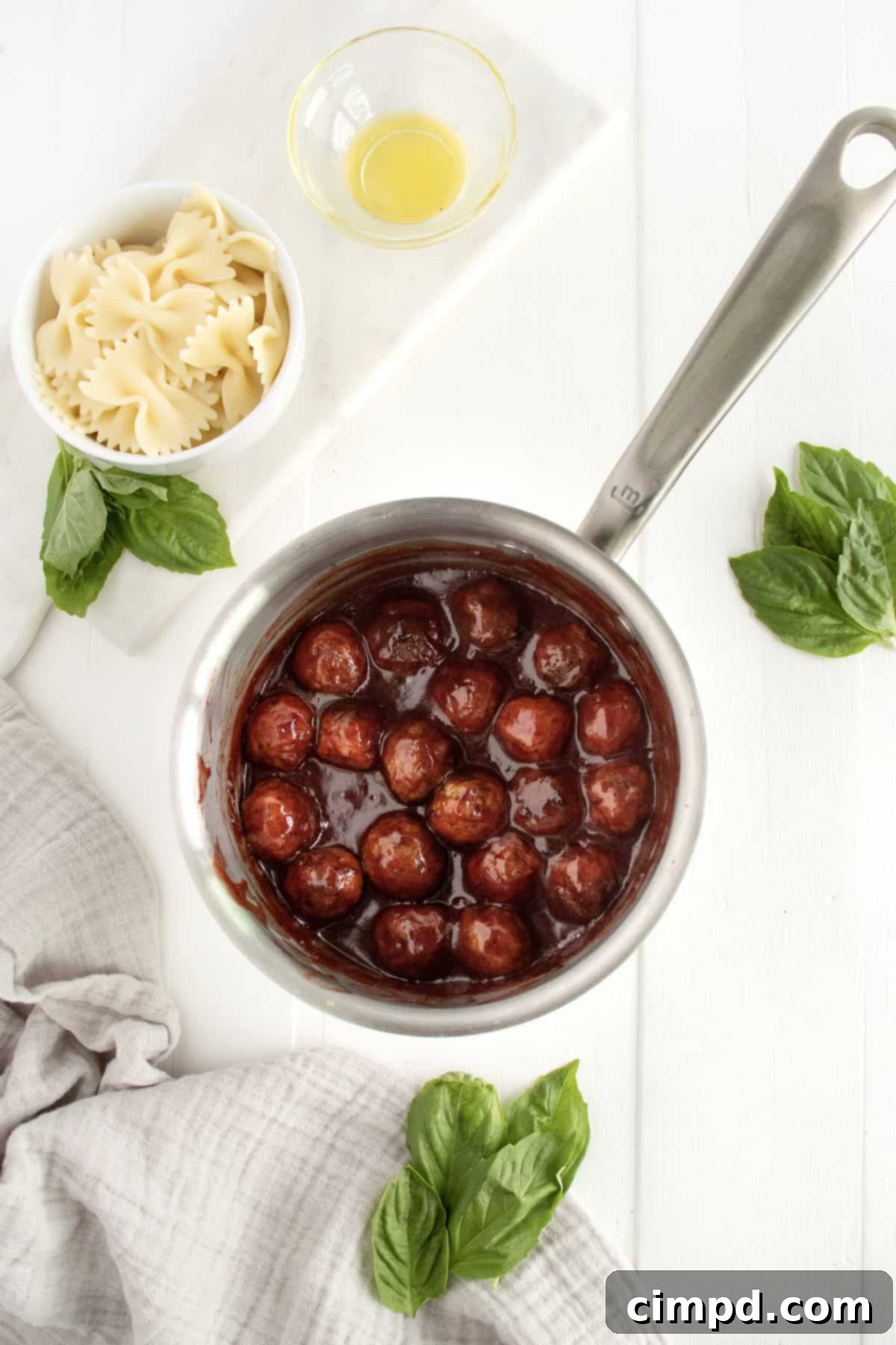 A vibrant close-up of delicious cocktail meatballs simmering in a rich, glossy sauce within a saucepan, ready to be paired with pasta for the skewers. The steam rising suggests freshness and warmth, inviting one to taste.