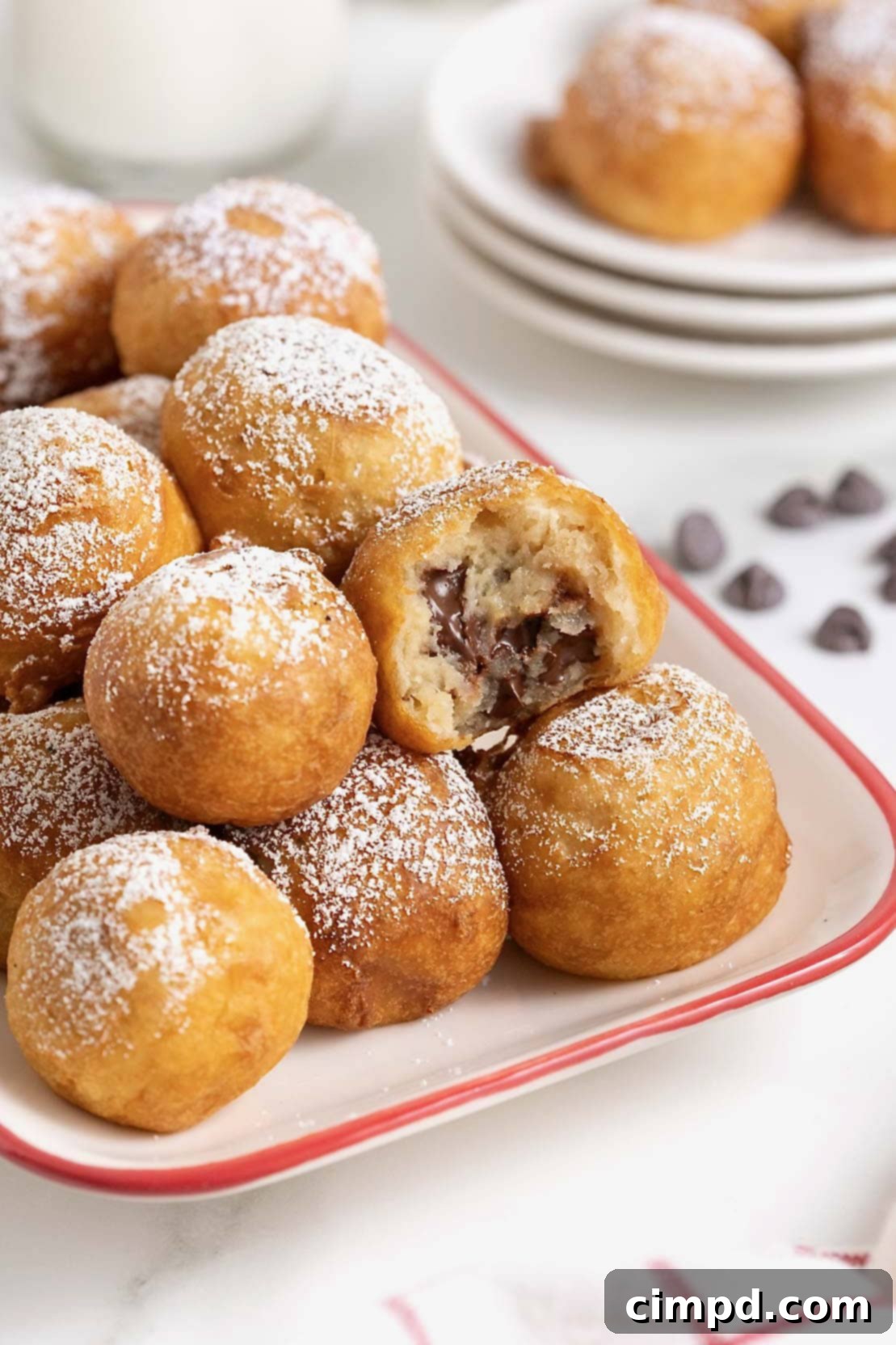 A beautiful white ceramic serving tray with a festive red border, generously filled with freshly prepared, golden-brown fried cookie dough bites, lightly dusted with powdered sugar.