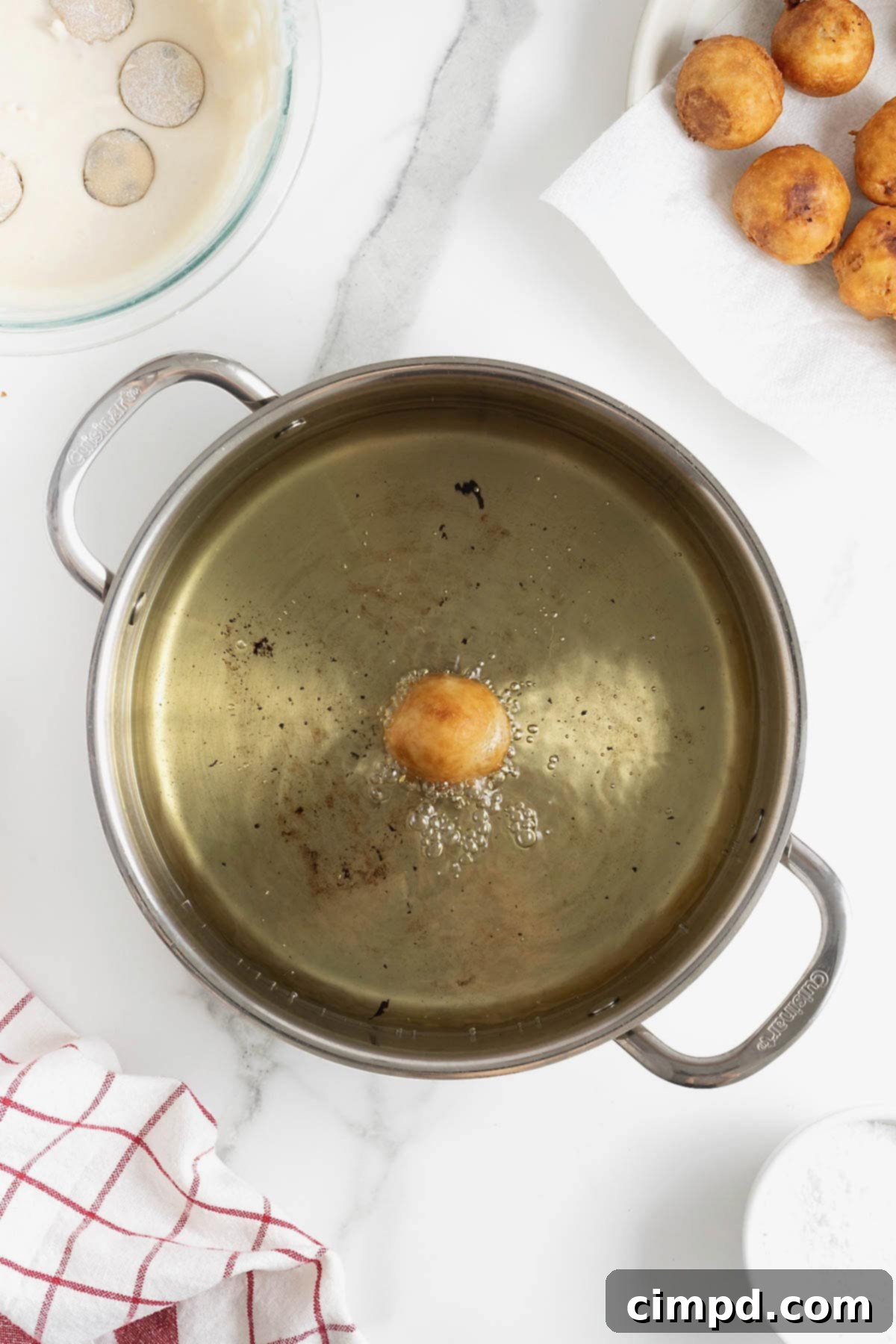 A large frying pan of hot oil prominently features a single deep-fried cookie dough ball, now golden brown and perfectly crisp, signaling its readiness.