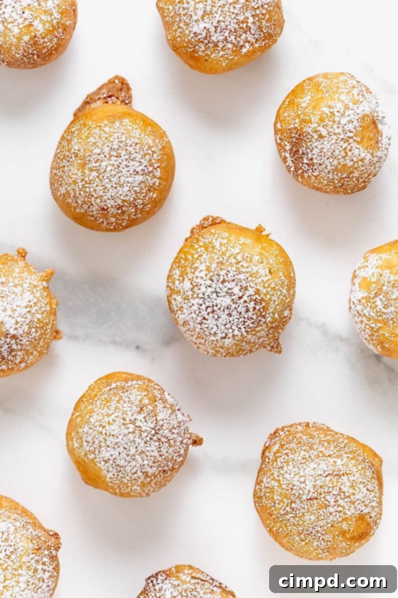 Several powdered sugar-dusted fried cookie dough bites are artfully arranged on a clean white marble counter, creating an elegant presentation of this sweet treat.