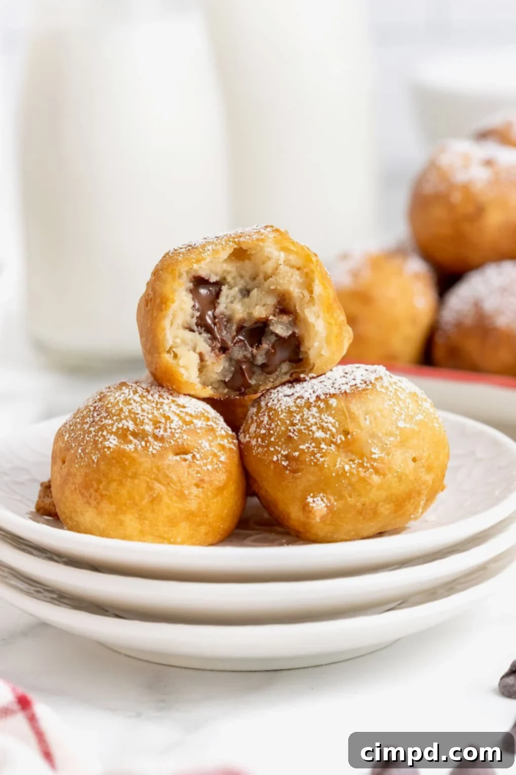 Three perfectly deep-fried chocolate chip cookie dough bites, dusted with powdered sugar, resting on a small, elegant white plate, ready to be enjoyed.