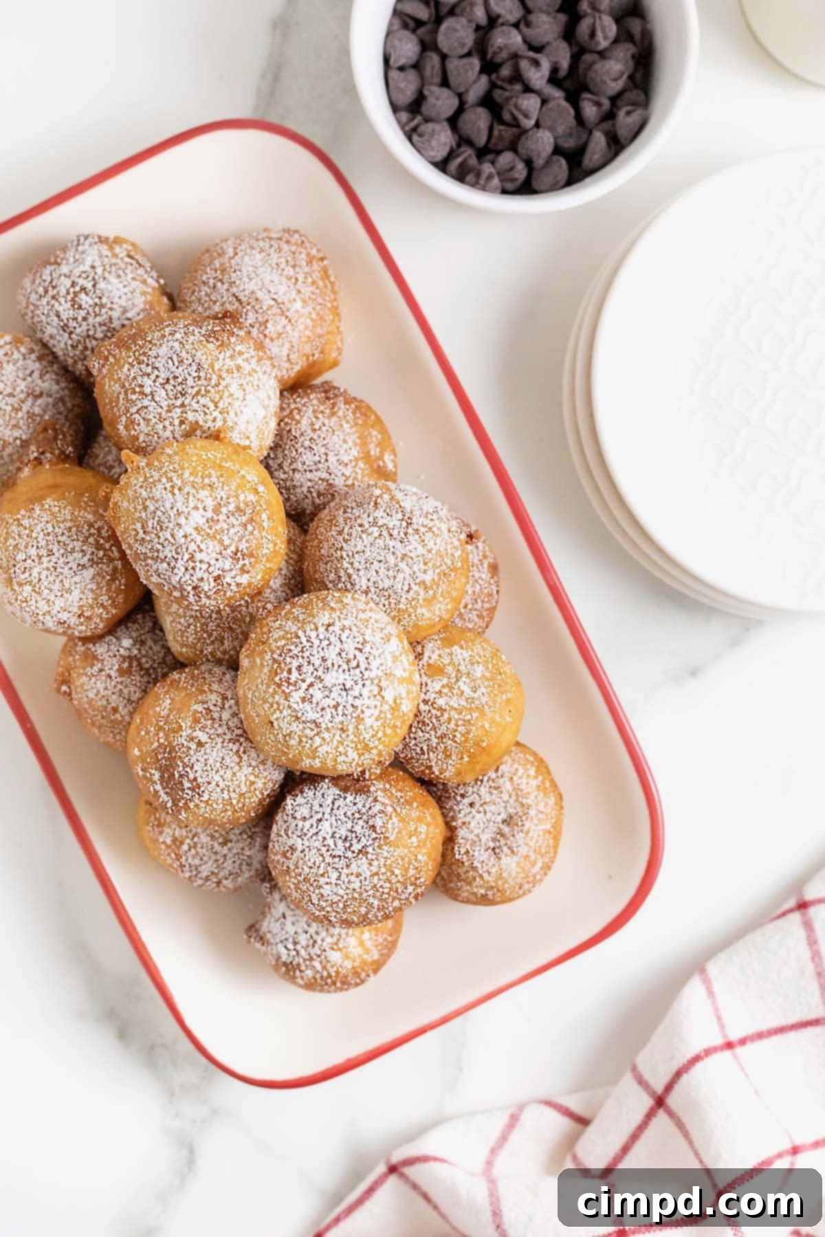 A festive white ceramic serving tray with a bright red border is generously filled with an assortment of golden-brown fried cookie dough pieces, each one a testament to indulgent dessert perfection.