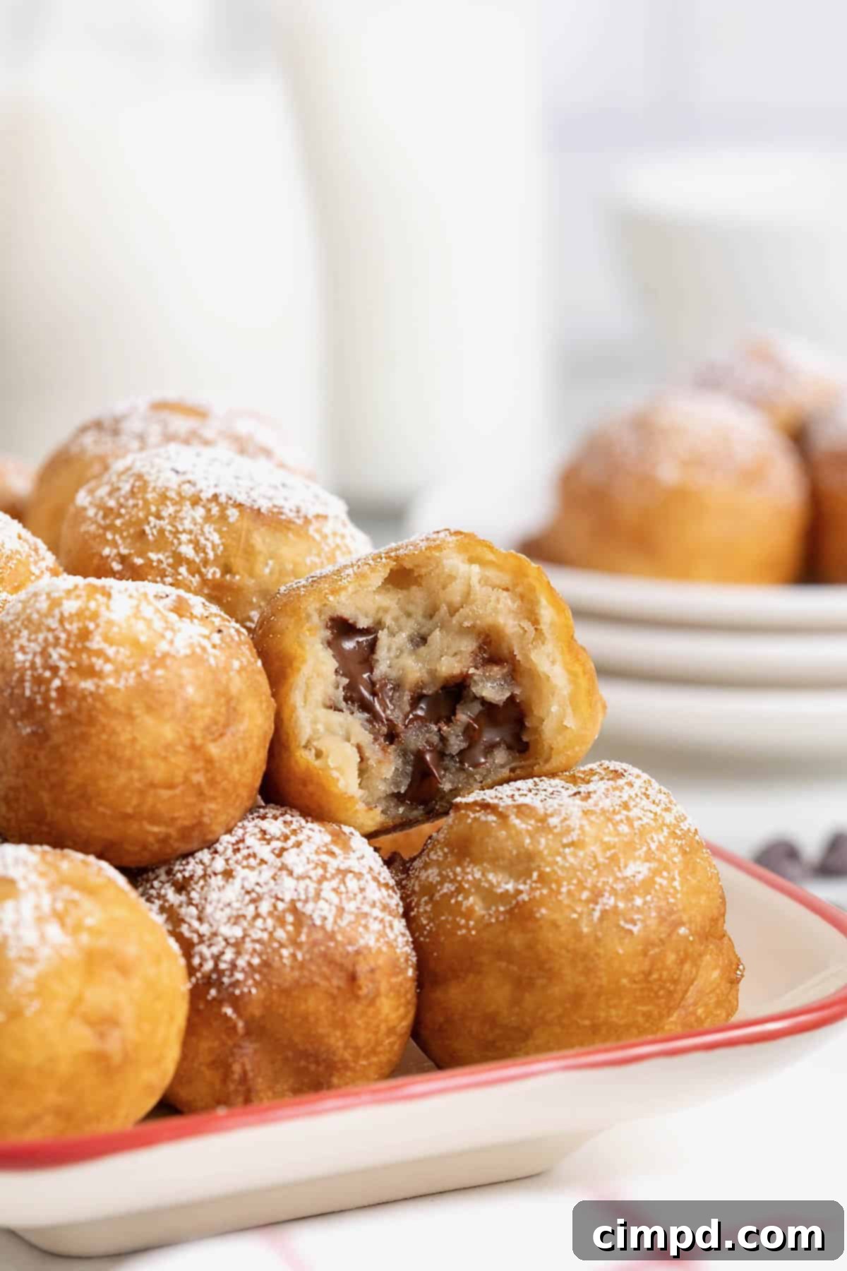 A vibrant white ceramic serving tray, accented with a striking red border, is brimming with an enticing collection of fried cookie dough bites, each perfectly golden and inviting.