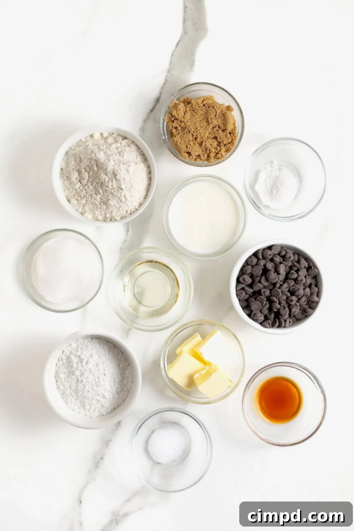 All the necessary ingredients for making delicious fried cookie dough are neatly arranged in small glass dishes on a pristine white marble counter, showcasing their readiness for preparation.