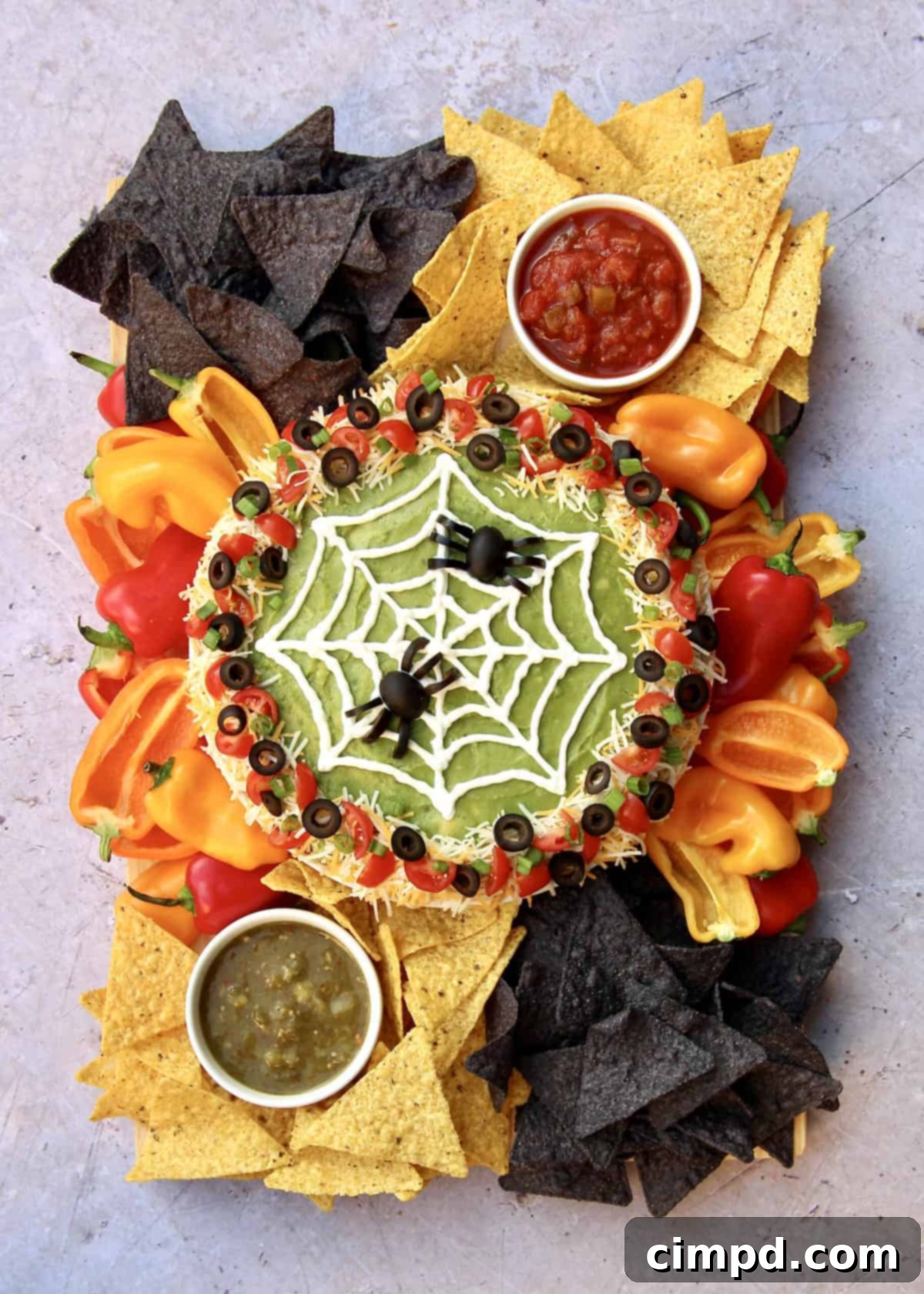 Spider Web Seven Layer Dip by The BakerMama - A festive Halloween appetizer board with a seven-layer dip decorated as a spiderweb and black olive spiders.
