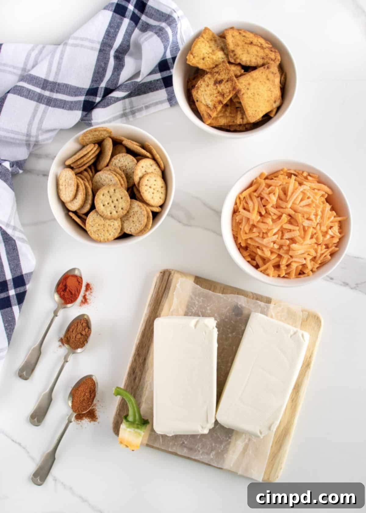 Ingredients to make a pumpkin cheese ball in white bowls on a white marble counter.