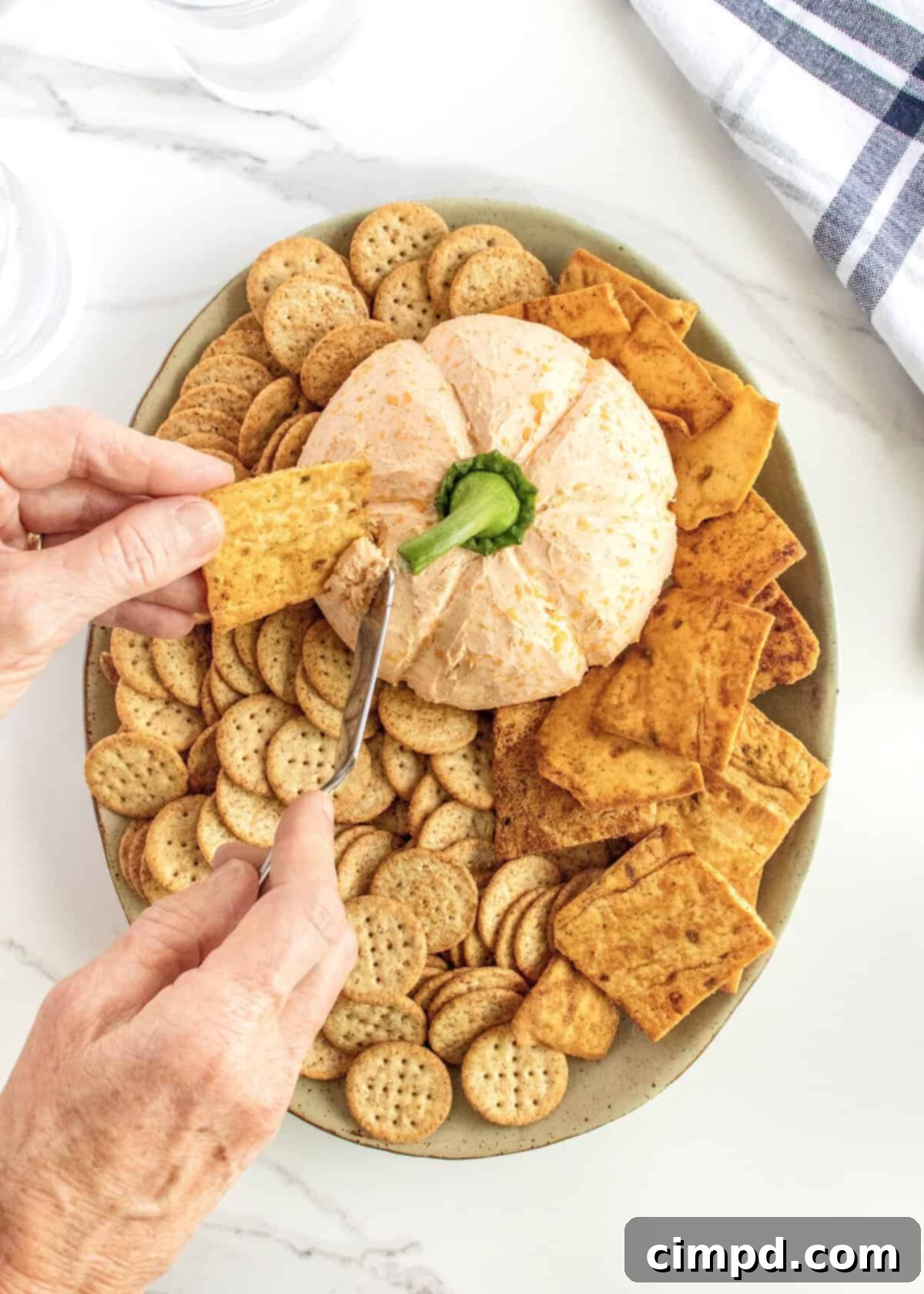 A hand using a knife to scrap pumpkin cheese ball onto a square cracker.