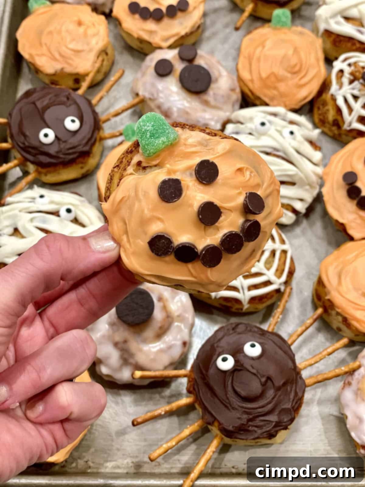 Close-up of three Halloween cinnamon rolls, a white ghost with chocolate chip eyes, an orange pumpkin with a gumdrop stem, and a chocolate spider with pretzel legs.
