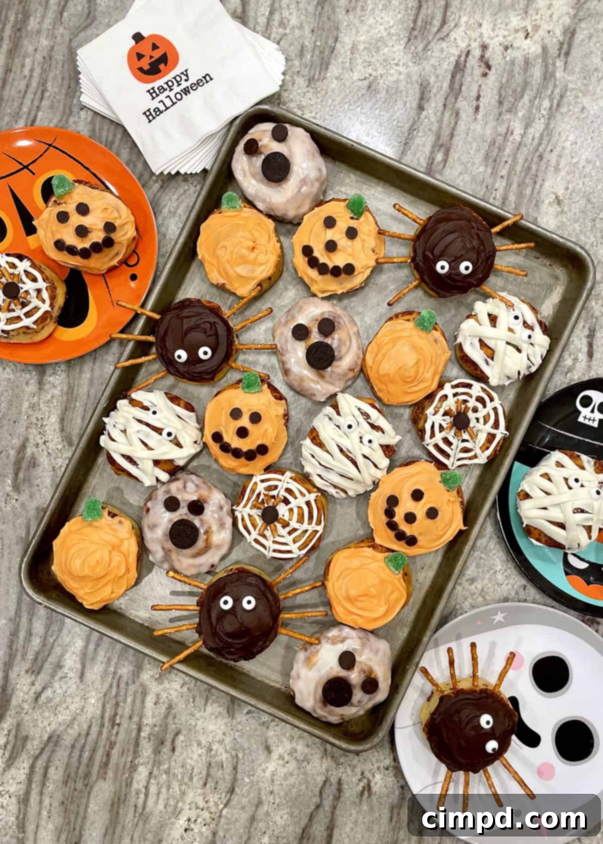 Assortment of ingredients for Halloween cinnamon rolls including various frostings, candy eyes, chocolate chips, and mini Oreos.