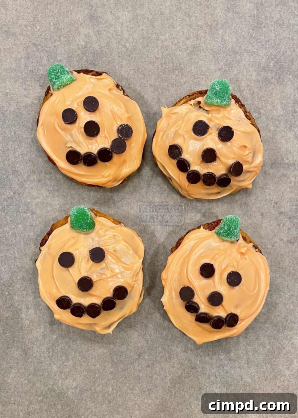 Three orange cinnamon rolls decorated as pumpkins and Jack-O'-Lanterns with green gumdrop stems and chocolate chip faces.