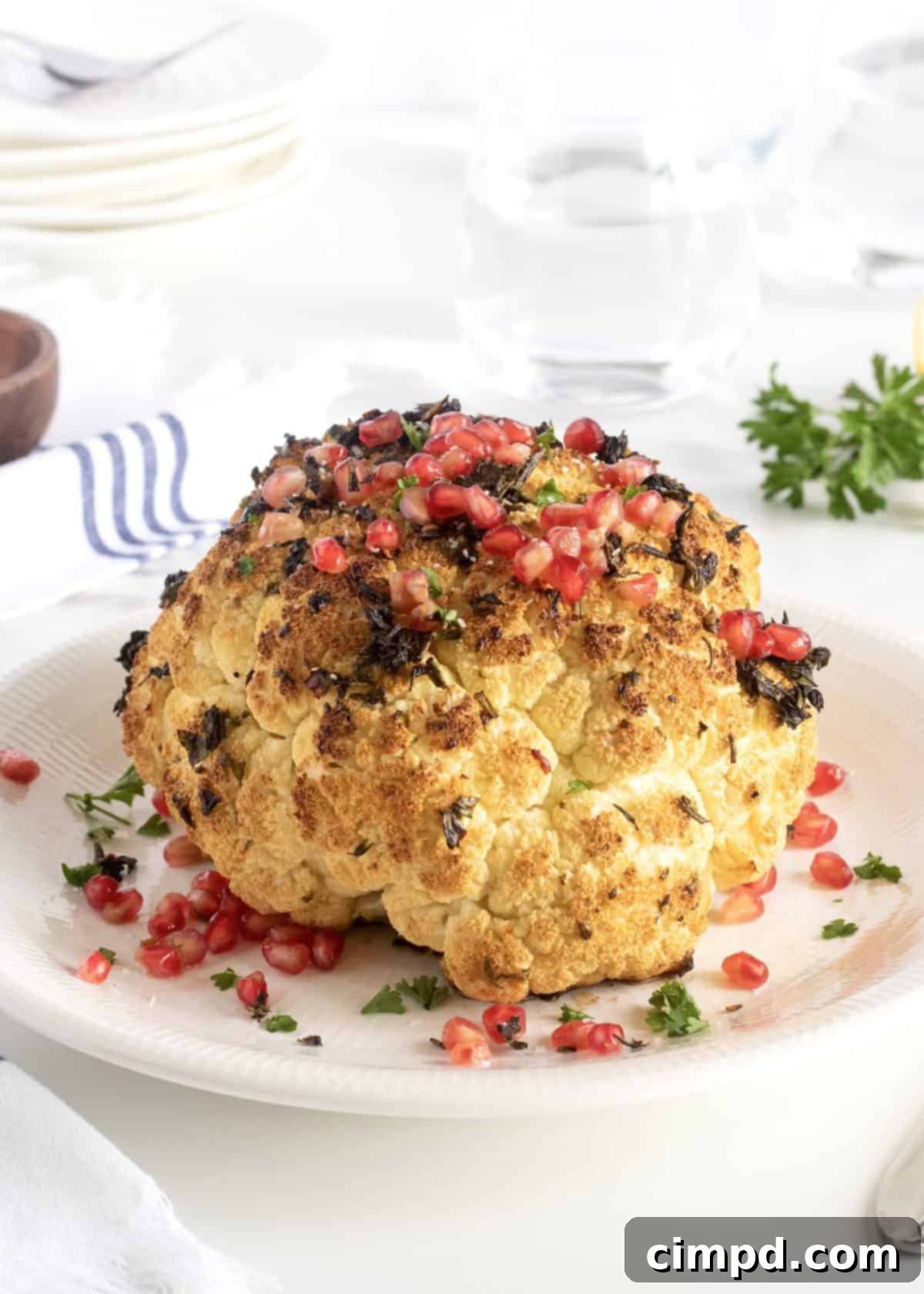 Beautifully roasted whole cauliflower garnished with fresh herbs and glistening pomegranate seeds, ready to serve.