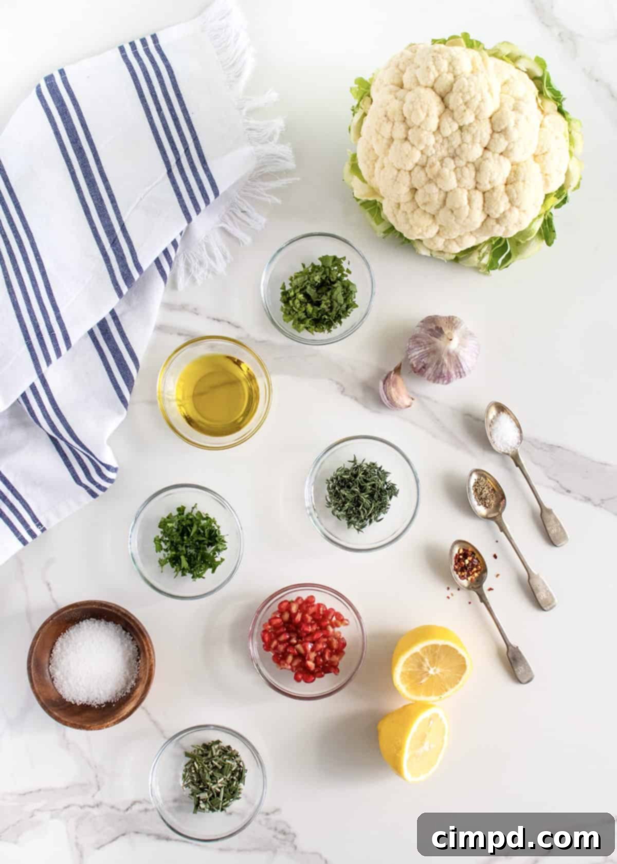 Fresh ingredients laid out: a whole cauliflower, various fresh herbs, garlic, and pomegranate seeds.