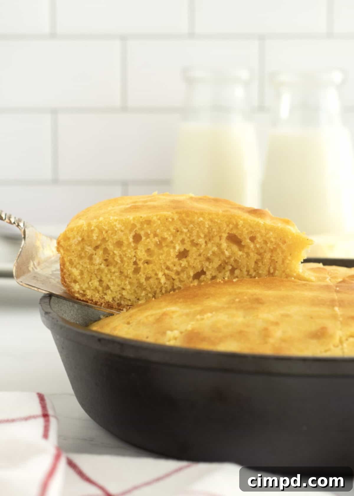 A slice of cornbread being lifted from a cast iron skillet on a metal spatula.