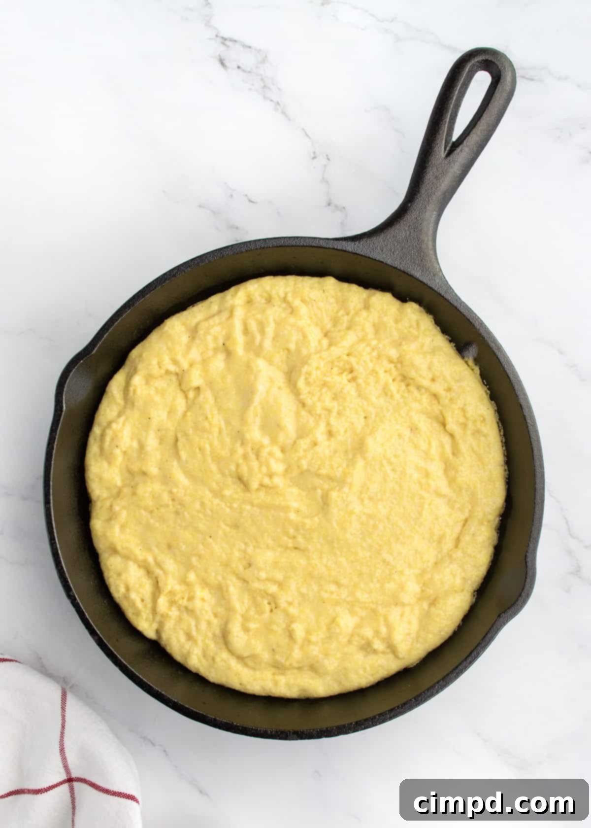 Cornbread batter in a cast iron skillet on a white marble counter.