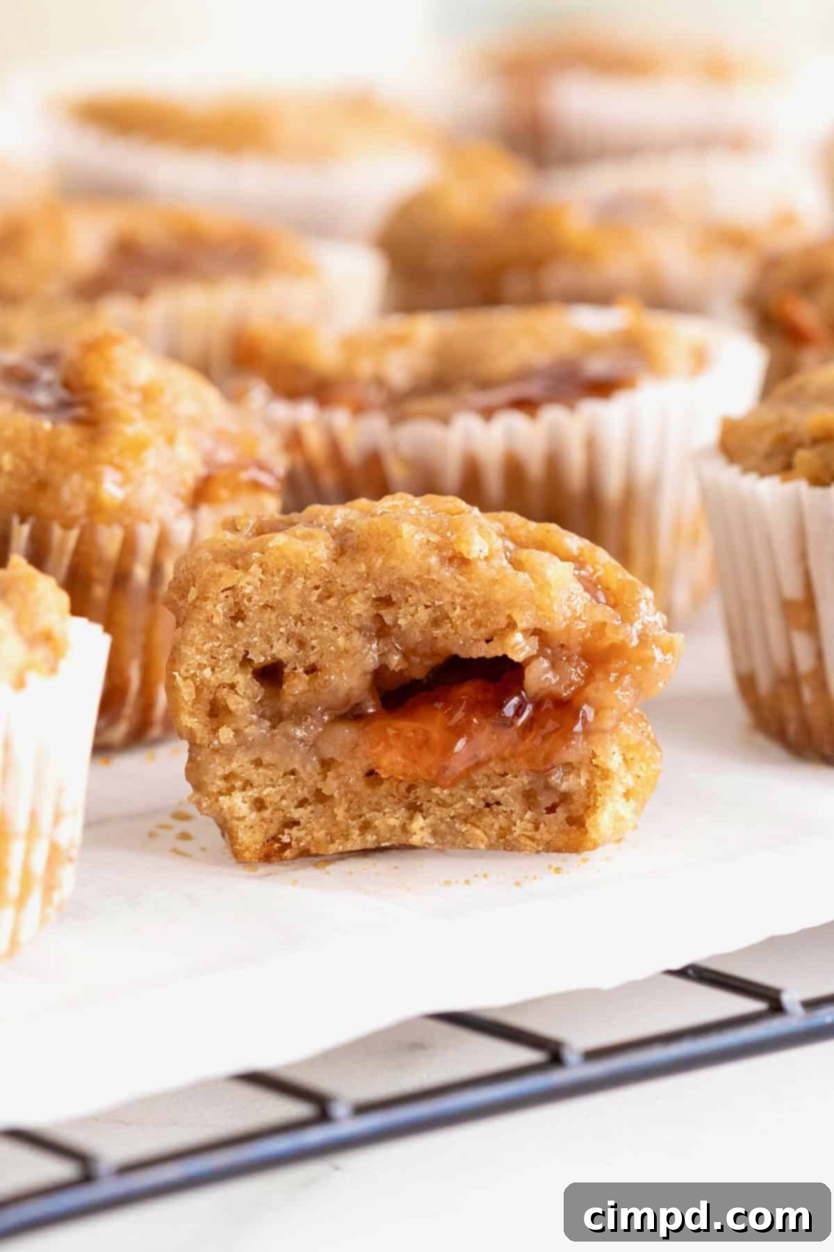 Peanut Butter and Jelly Muffin Bites 3 Peanut butter and jelly muffins on a parchment lined cooling rack. The front-most muffin is cut in half revealing the jelly center.
