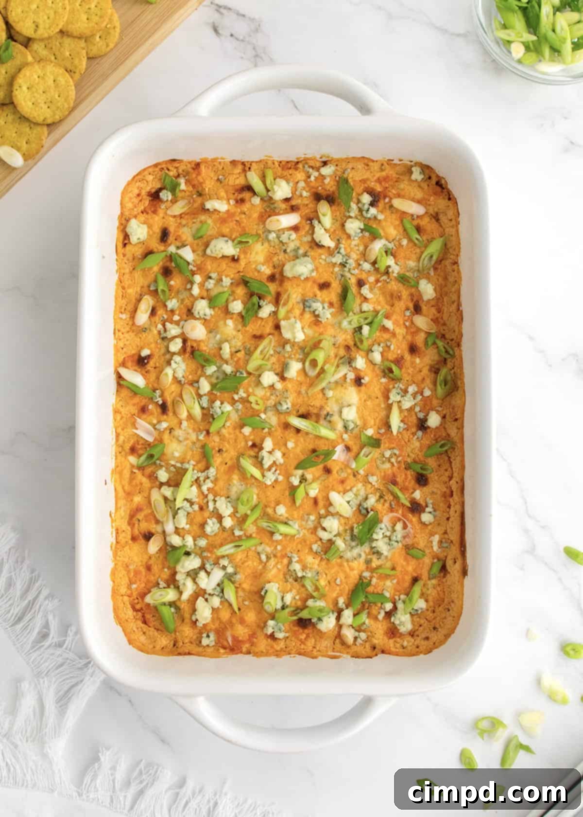 Ultimate Buffalo Chicken Dip 2 Creamy and delicious Buffalo Chicken Dip in a baking dish, garnished with fresh green onions and blue cheese crumbles, ready for serving.