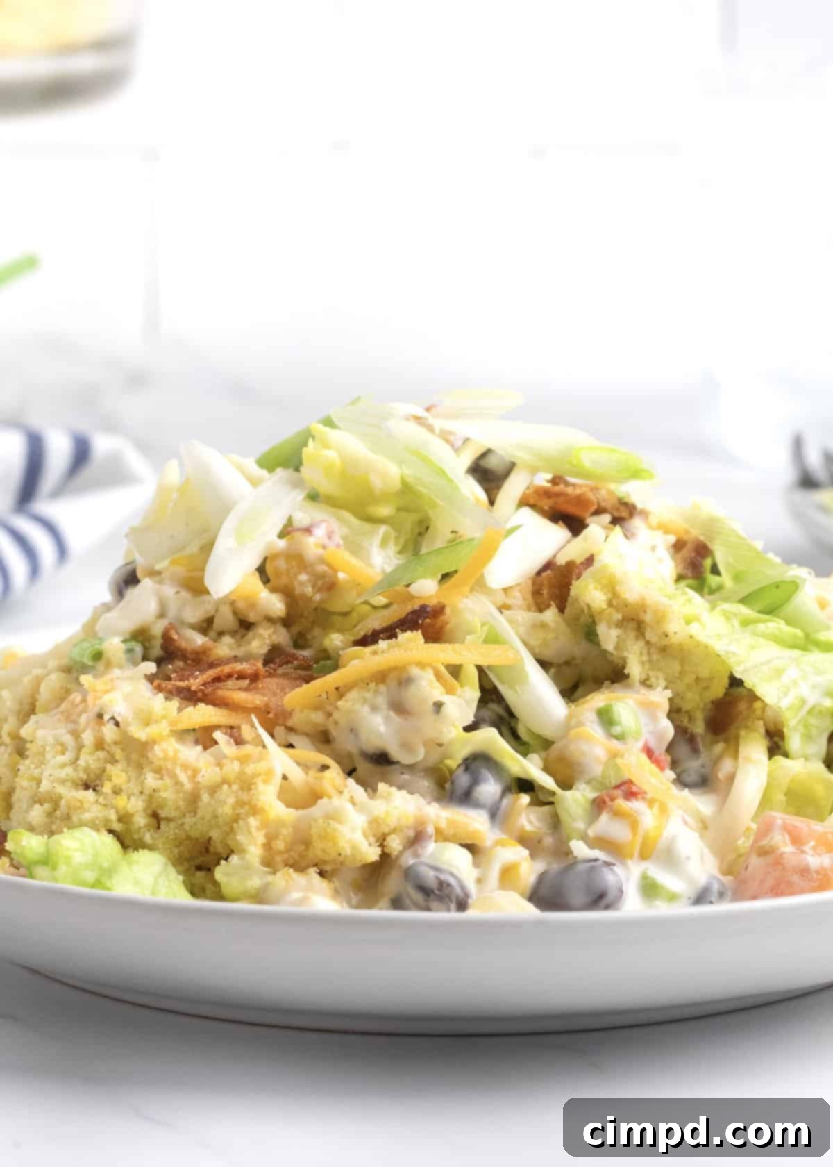 Southern Stacked Cornbread Medley 7 A single serving of cornbread salad on a white ceramic plate, with a blue and white cloth napkin in the background.