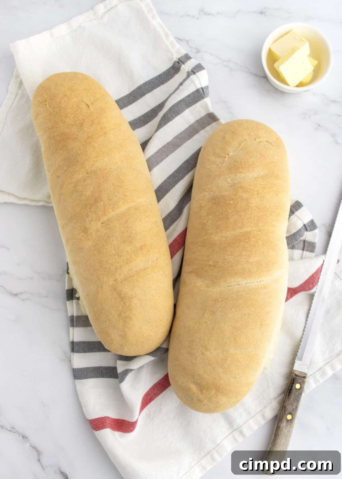 A beautifully baked loaf of 5-Ingredient Homemade French Bread by The BakerMama, showcasing its rich golden crust and inviting texture on a wooden surface.