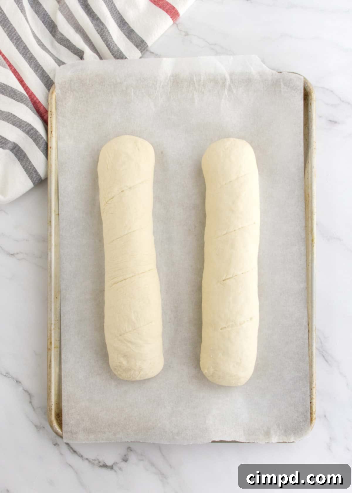 Two shaped loaves of 5-Ingredient Homemade French Bread, meticulously formed and placed on a baking sheet, ready for the final proofing and baking.