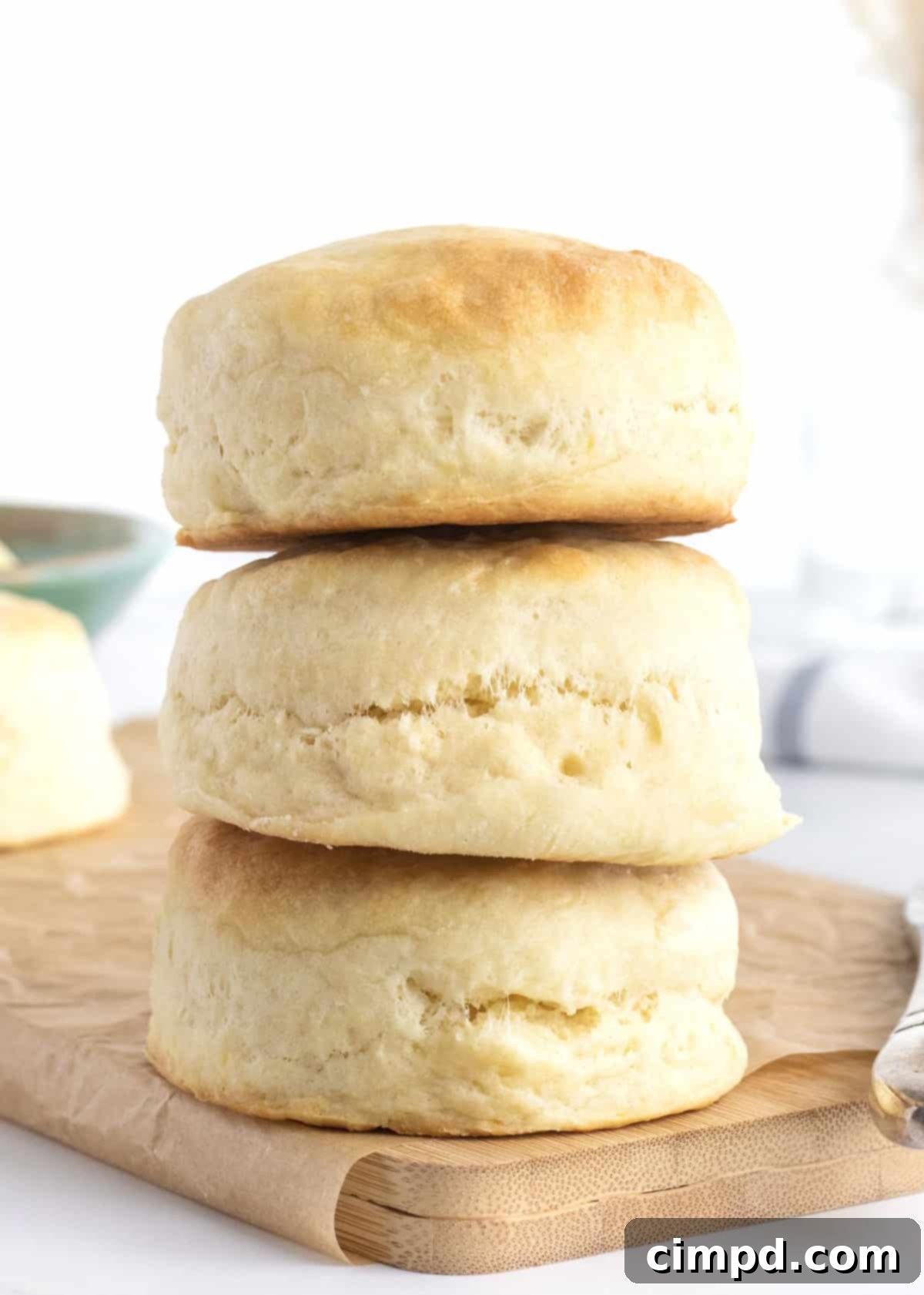 Heavenly Fluffy Biscuits 4 Three perfectly baked Angel Biscuits stacked artfully on a rustic wooden cutting board, ready for serving.