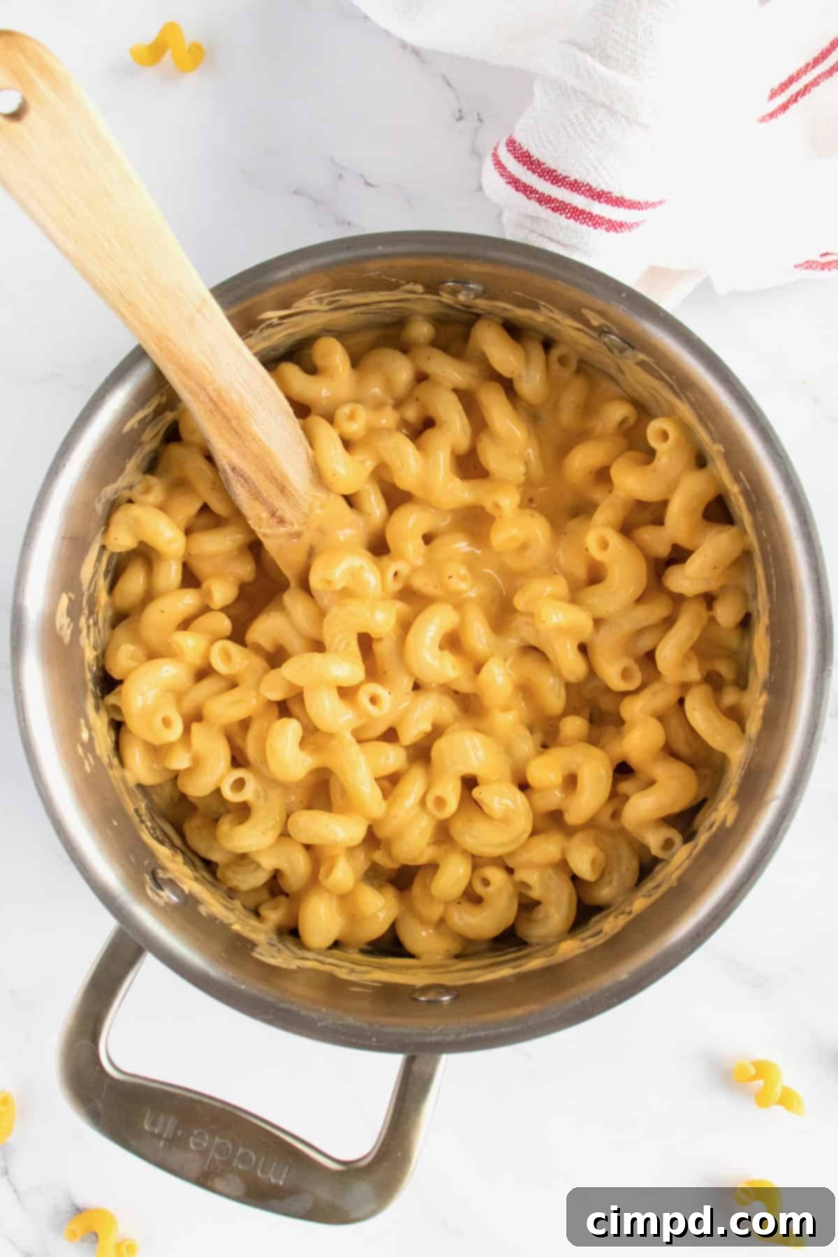 A pot of golden, creamy stovetop macaroni and cheese with a wooden spoon in it, ready to be served.