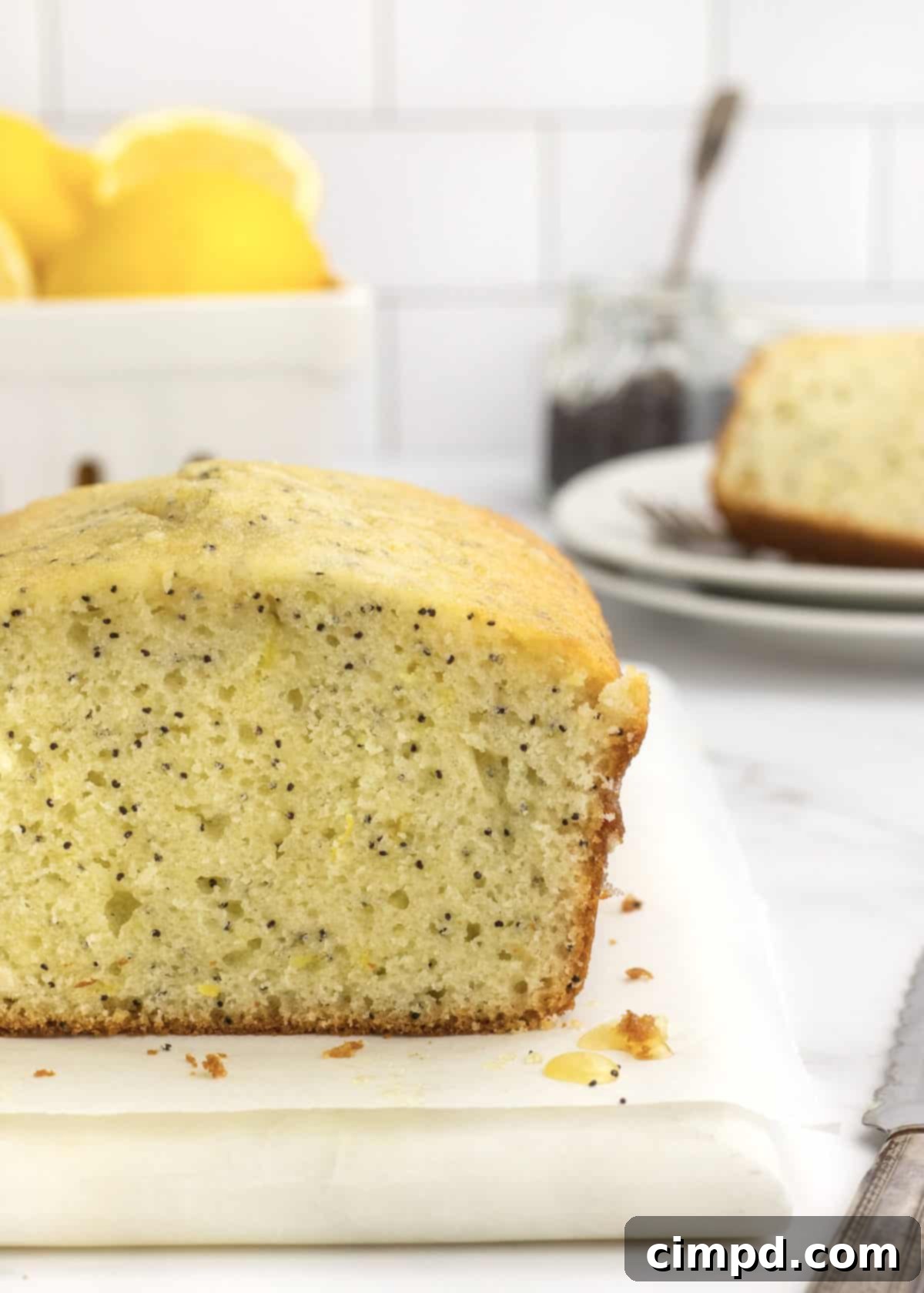A vibrant, close-up shot of a Lemon Poppy Seed Bread loaf, showcasing its texture and glaze, by The BakerMama