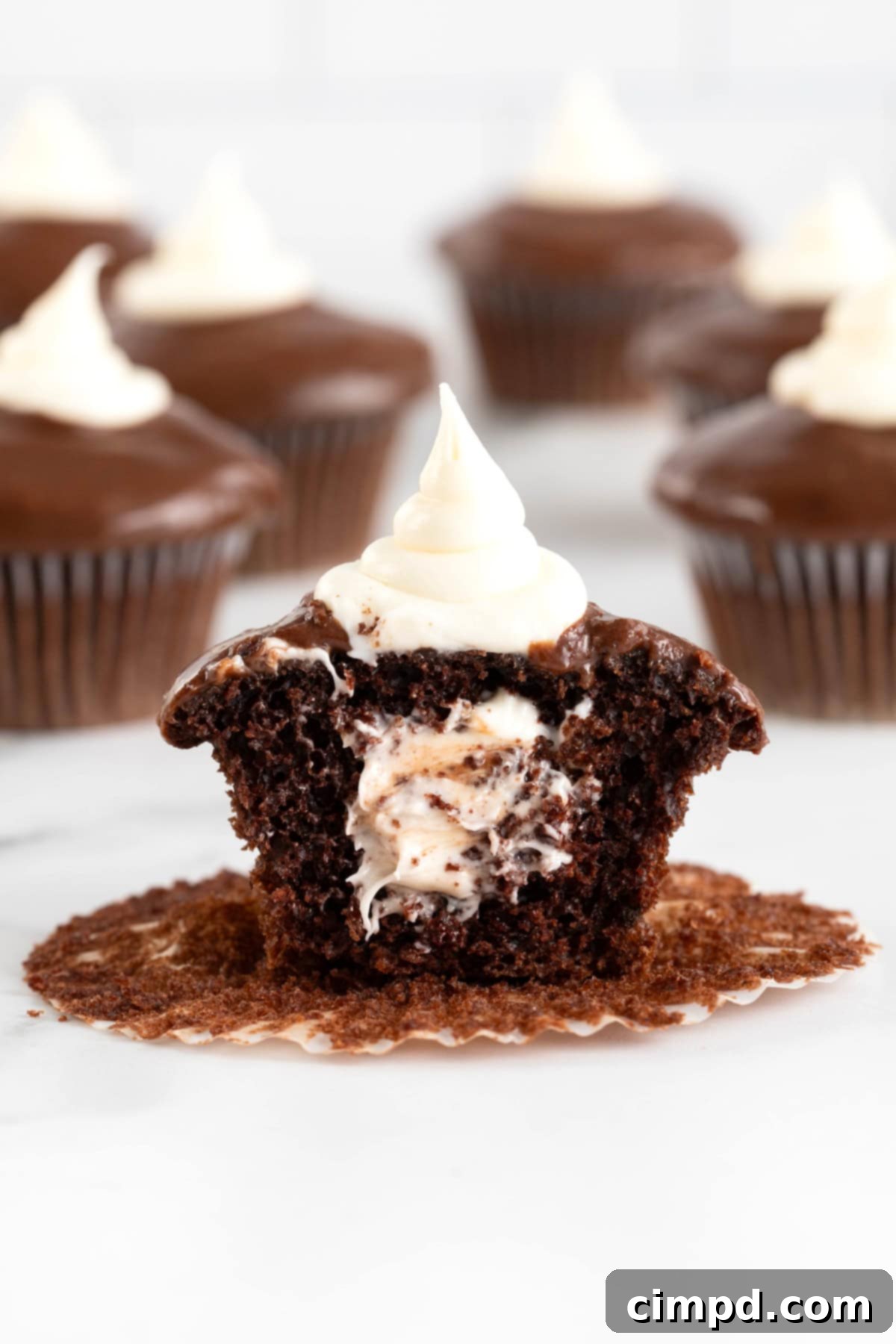 A chocolate cupcake with a cream center topped with chocolate ganache and cream, presented beautifully on a clean surface.