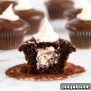 A chocolate cupcake with a cream center topped with chocolate ganache and cream.
