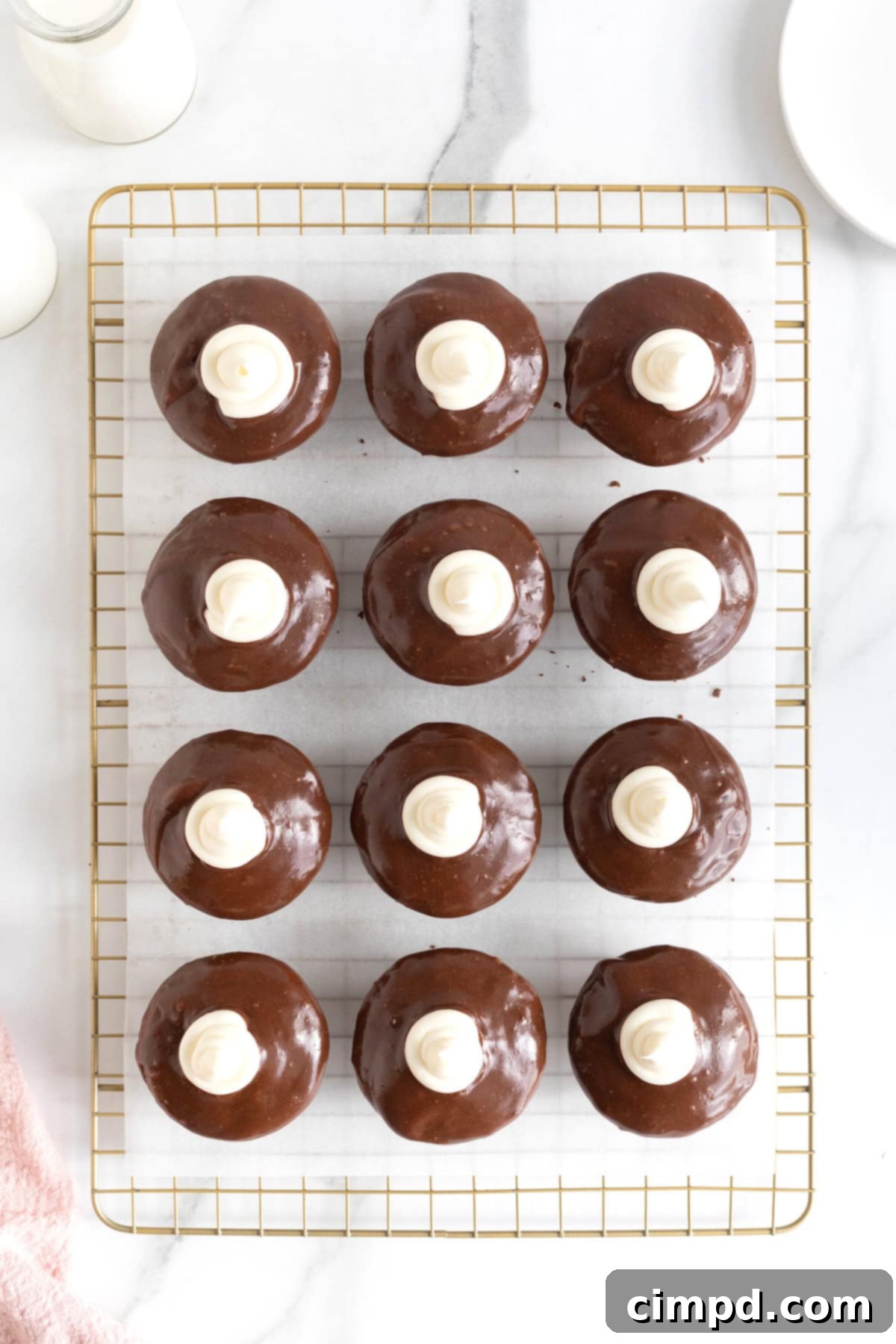 Twelve dark chocolate cupcakes, beautifully topped with chocolate ganache and marshmallow cream, arranged on a parchment-lined gold tone cooling rack.