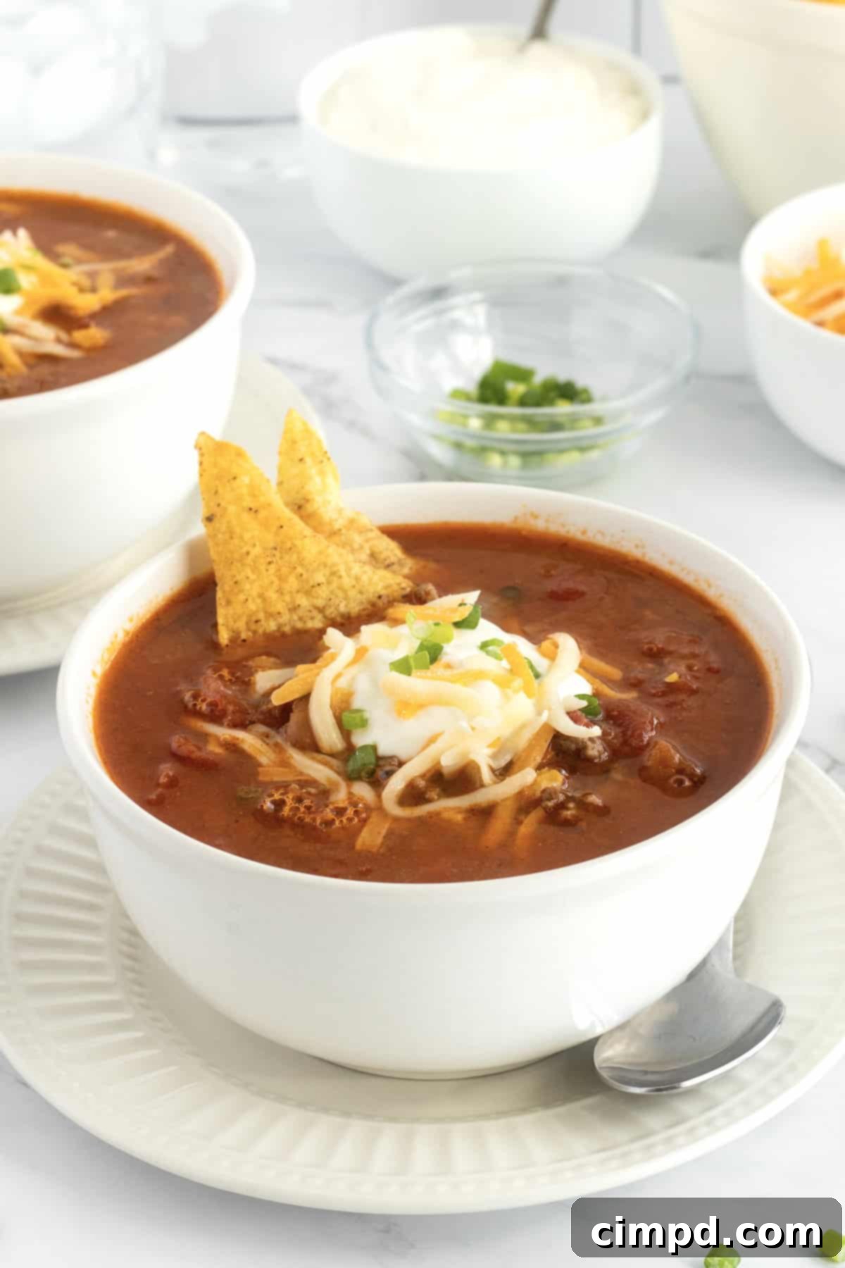 A white ceramic bowl filled with delectable taco soup, topped with creamy sour cream and shredded cheese.