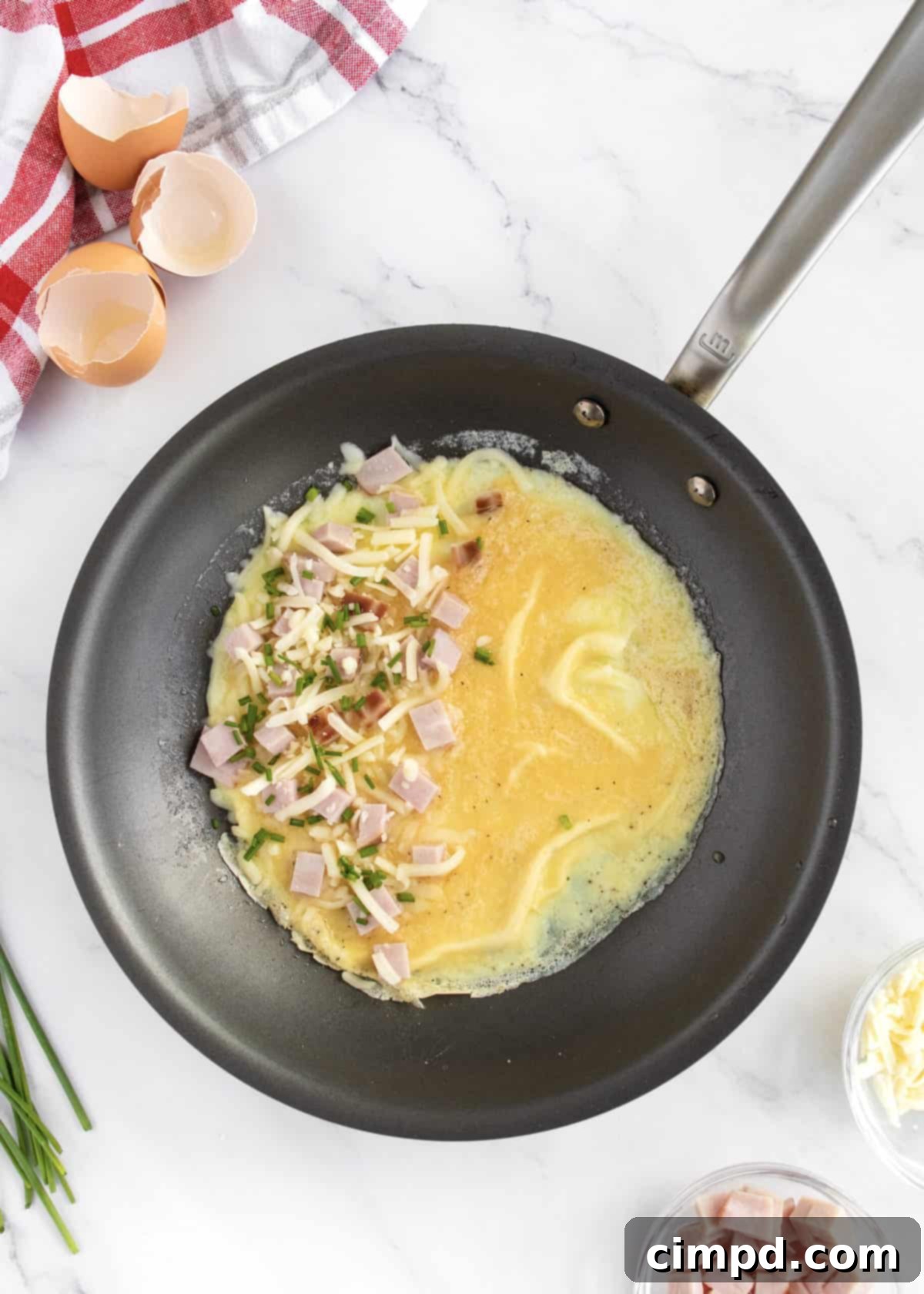 The Ultimate Omelet Guide 6 Adding delicious fillings to one half of a cooking omelet in a skillet.