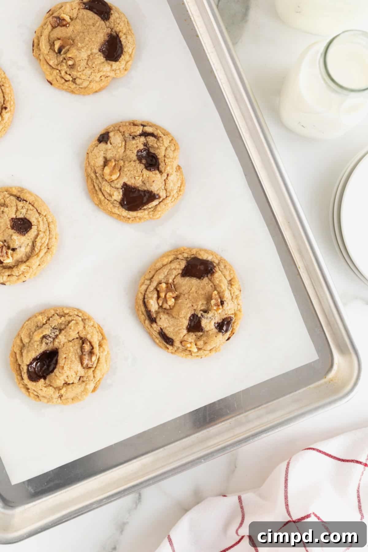 Six dark chocolate walnut cookies on a parchment lined baking sheet.