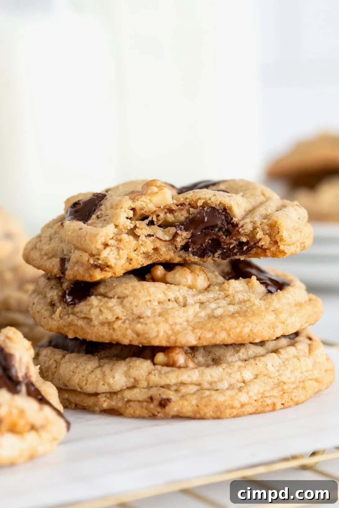 A stack of three dark chocolate chunk walnut cookies on a white surface. The top cookie has a bite out of it.