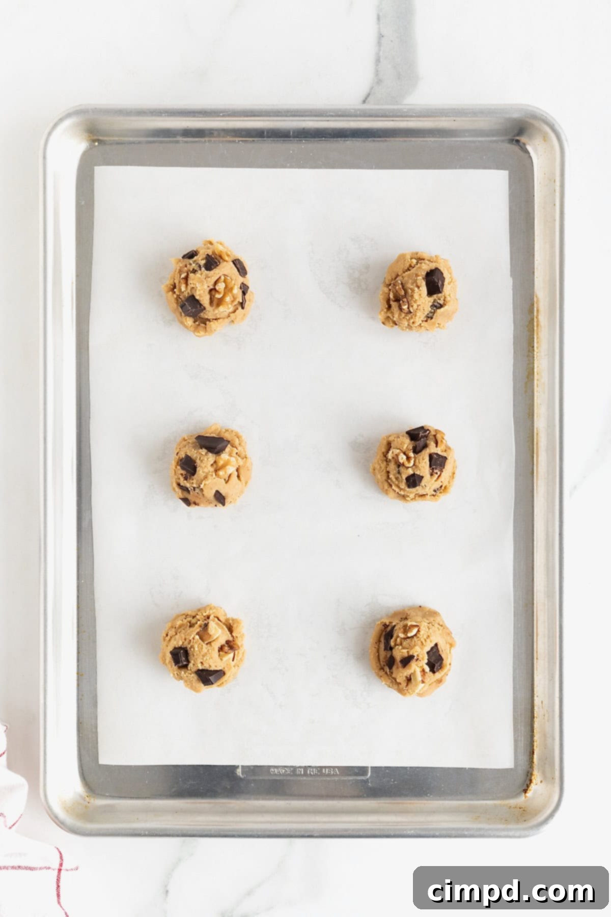 Six dark chocolate walnut cookie dough balls on a parchment lined aluminum baking sheet.