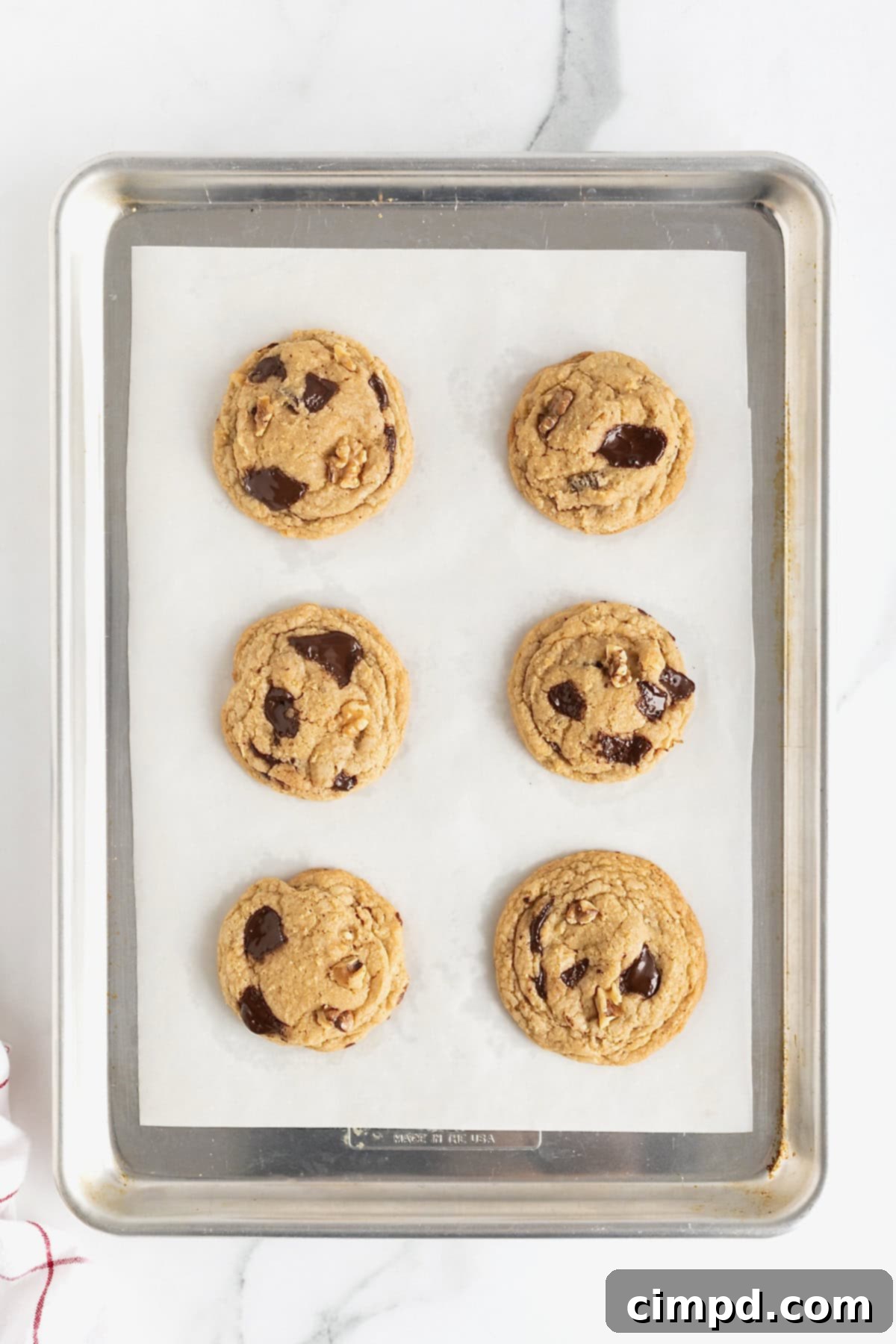 Six dark chocolate walnut cookies on a parchment lined aluminum baking sheet.