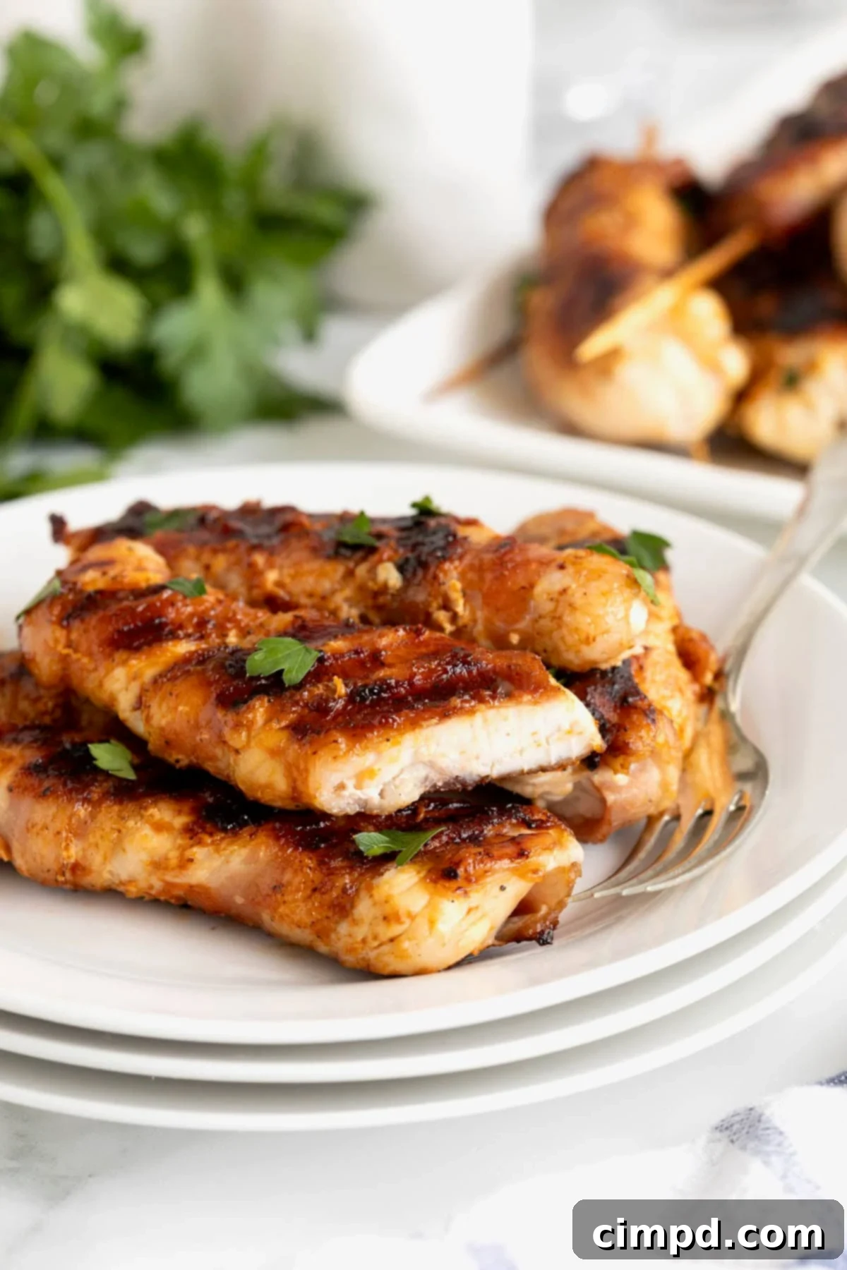 Crispy Bacon Chicken Skewers 3 A small white plate piled high with golden brown bacon-wrapped chicken skewers, garnished with fresh herbs.