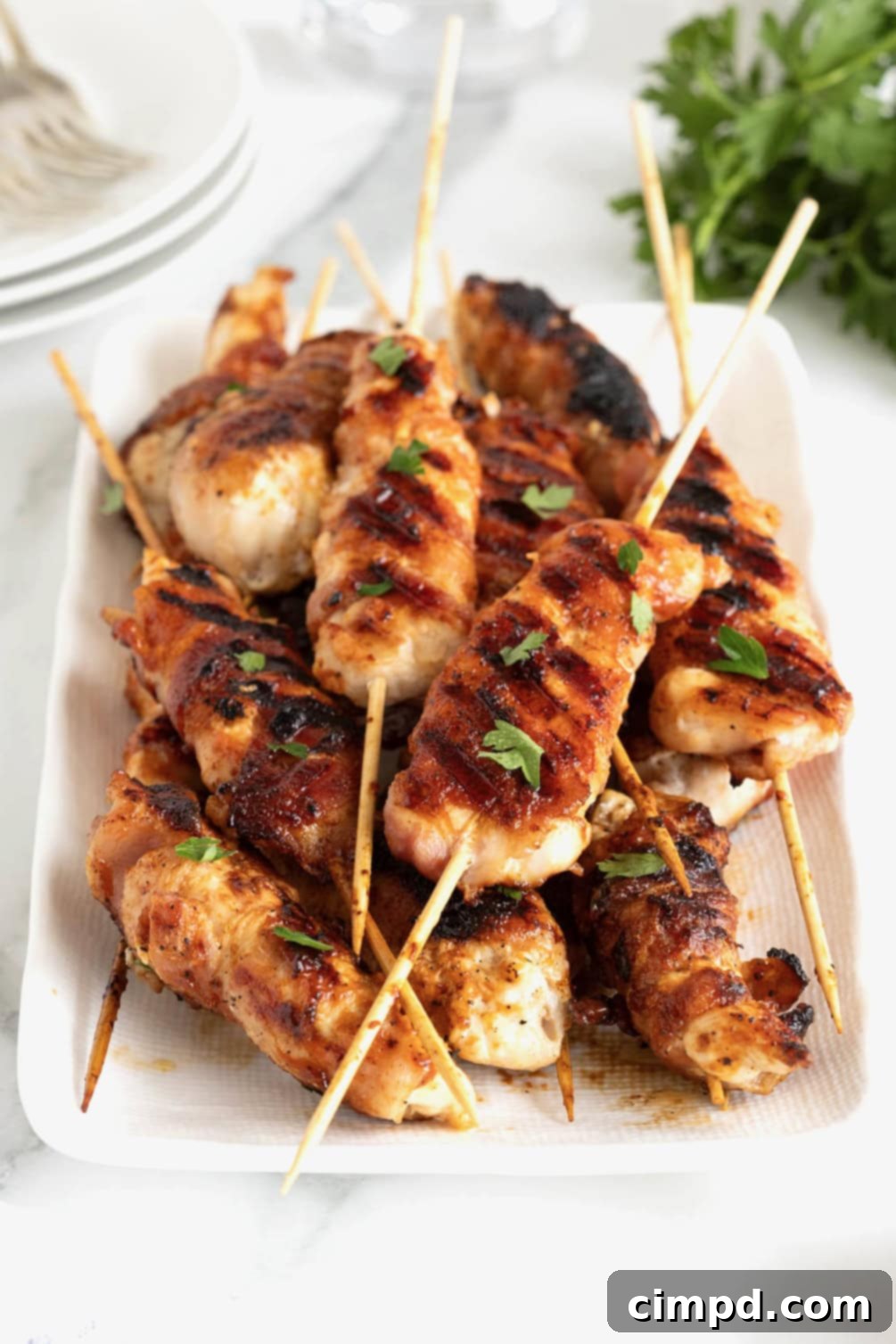 Crispy Bacon Chicken Skewers 5 A rectangular white serving platter filled with numerous grilled chicken skewers on bamboo sticks.