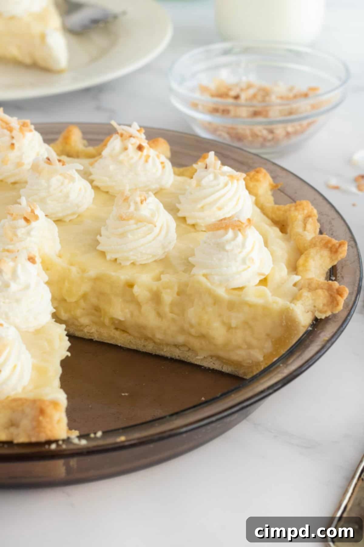 A whole Coconut Cream Pie, covered with plastic wrap, chilling in the refrigerator