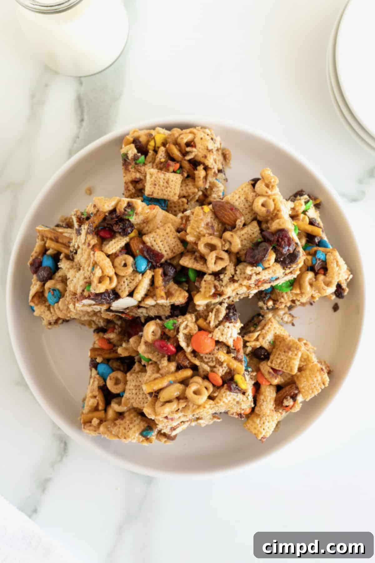 No-Bake Grab-and-Go Bars 2 Snack bars made with cereal, pretzel sticks and M&M's on a white plate, showcasing their delightful texture and colorful additions.