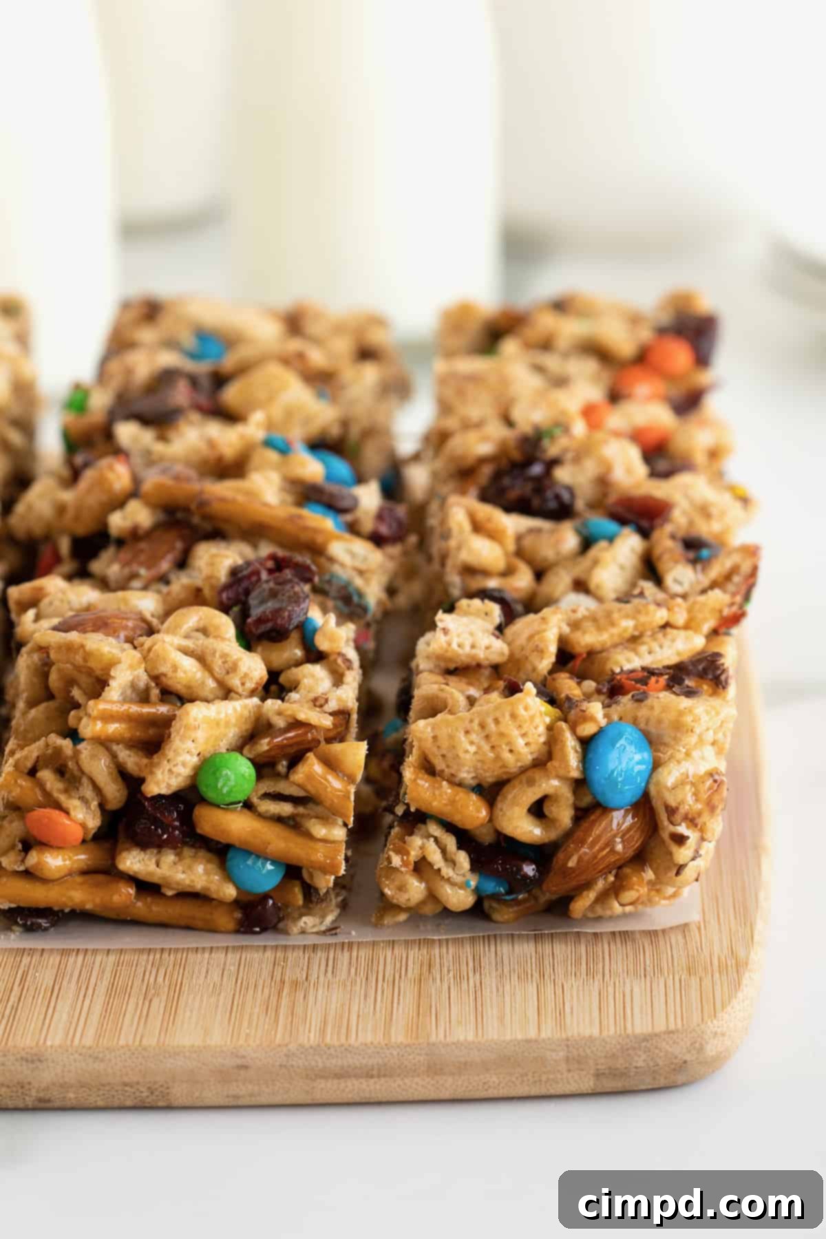 No-Bake Grab-and-Go Bars 9 A stack of golden brown snack bars, made with cereal, pretzel sticks, and M&M's, neatly arranged on a wooden cutting board.