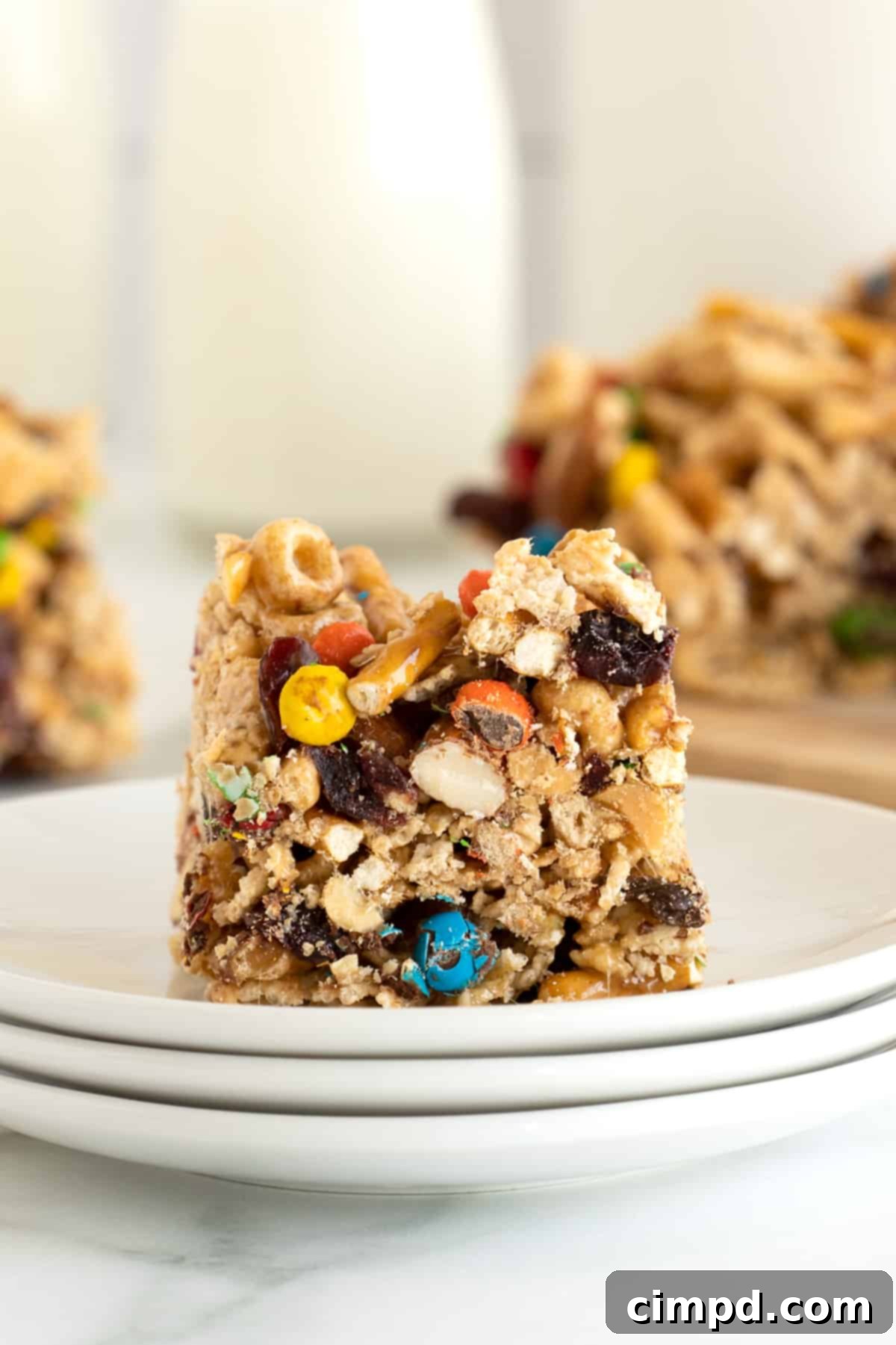 No-Bake Grab-and-Go Bars 3 A close-up view of a single no-bake cereal snack bar, topped with colorful M&Ms and various nuts, resting on a white plate.