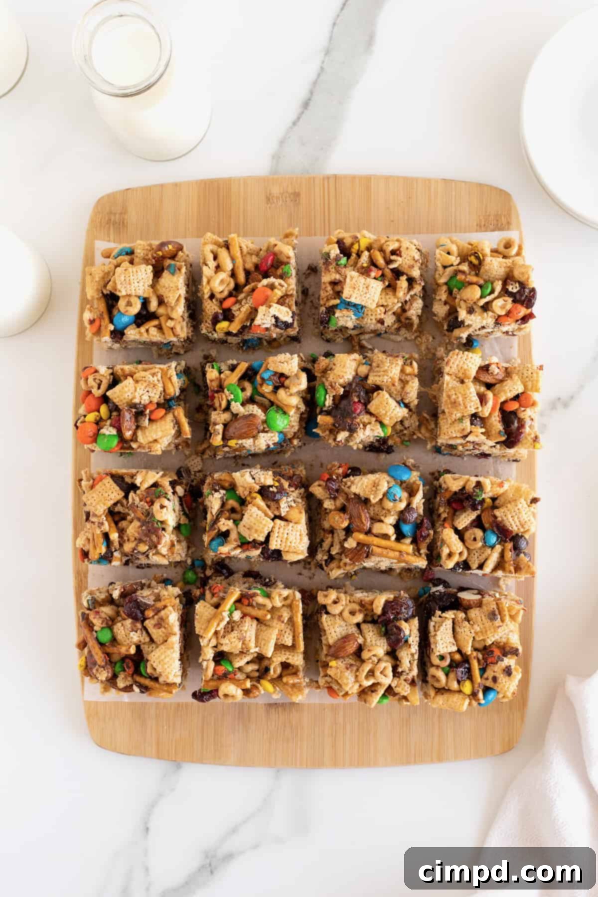 No-Bake Grab-and-Go Bars 8 Freshly cut no-bake snack bars, featuring a delightful blend of cereal, pretzel sticks, and M&M's, arranged on a natural wooden cutting board.