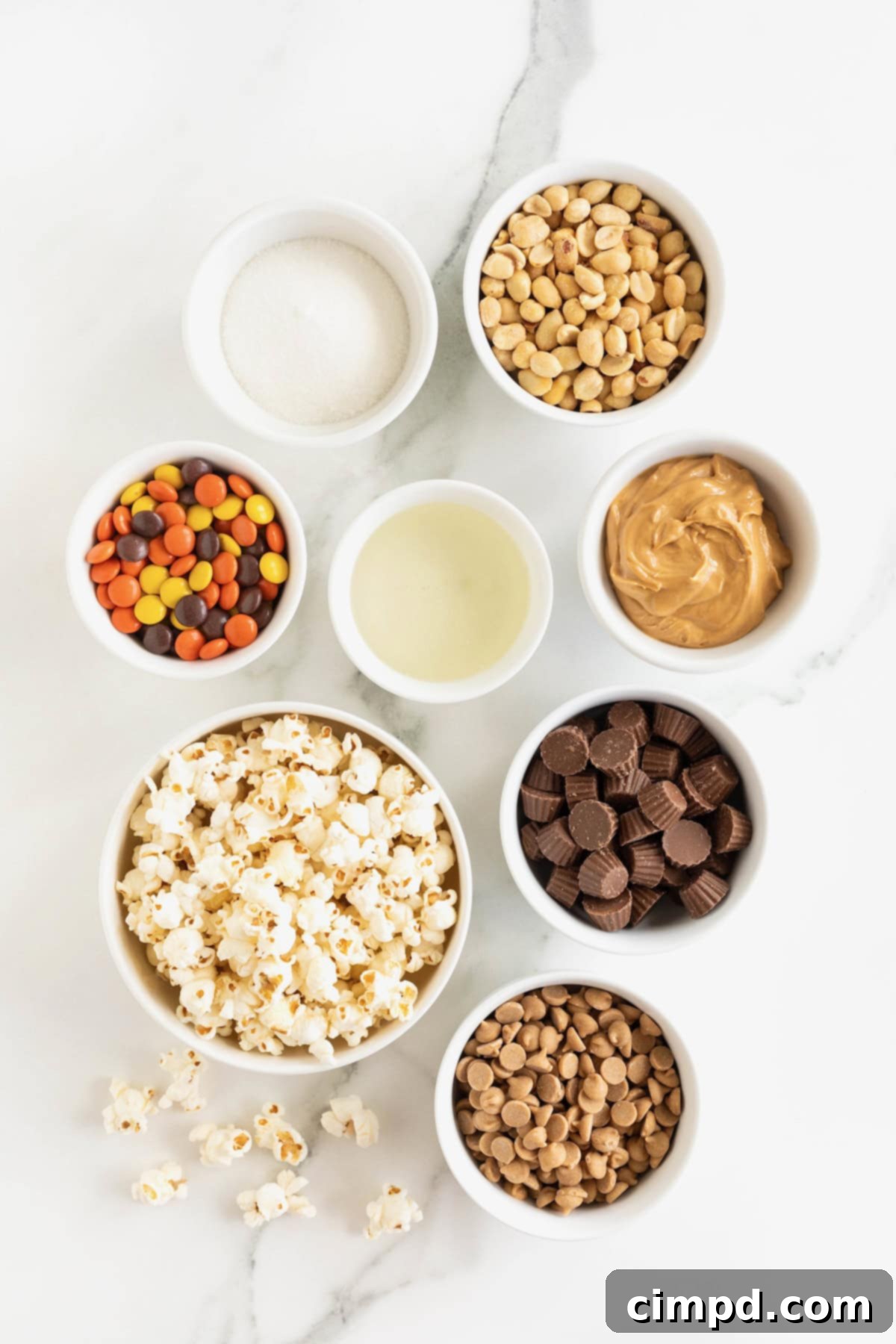 Ingredients for loaded peanut butter popcorn balls in small glass dishes a white marble counter.