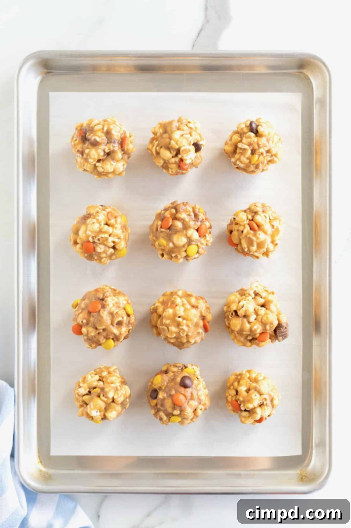 12 peanut butter popcorn balls on a parchment lined baking sheet.